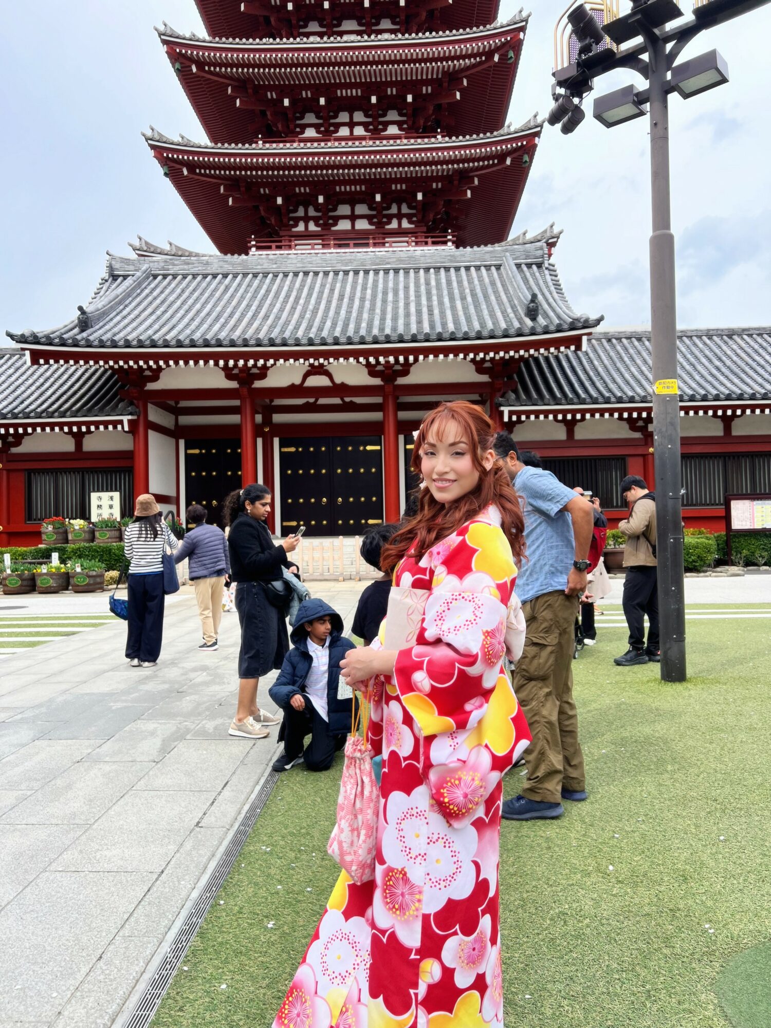 Woman in colorful floral dress standing in front of a traditional multi-tiered pagoda with people nearby.