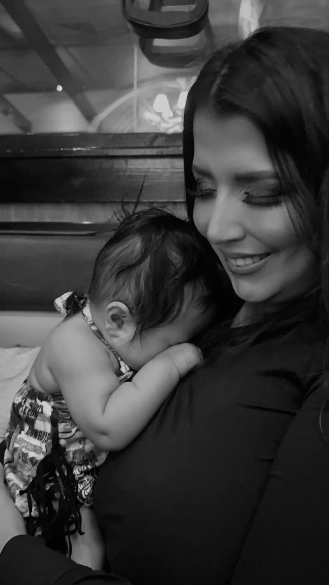 Woman holding a sleeping child close, both smiling gently, in black and white.