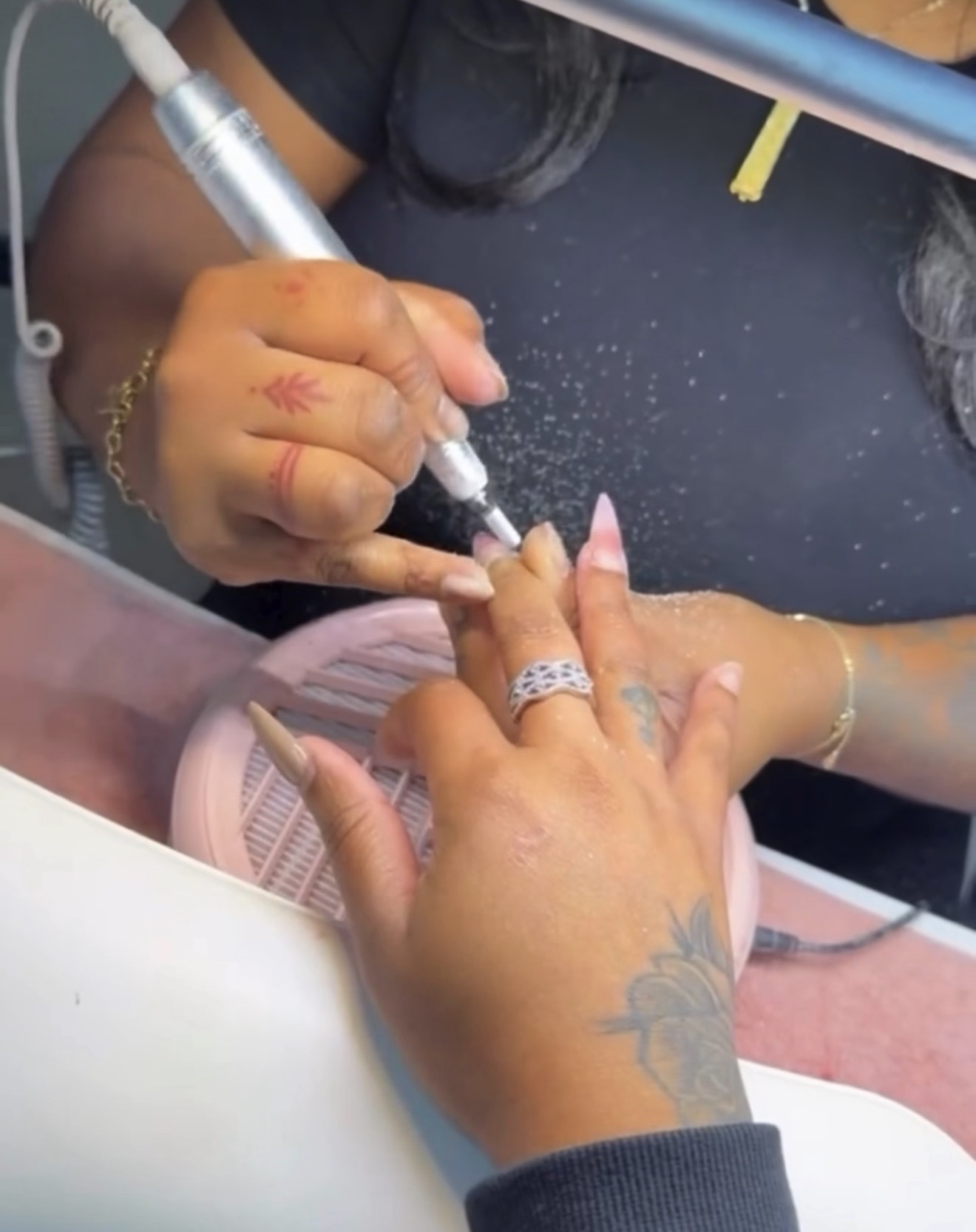Person receiving a manicure, with a technician applying nail polish or treatment to their fingernails, hands resting on a surface.