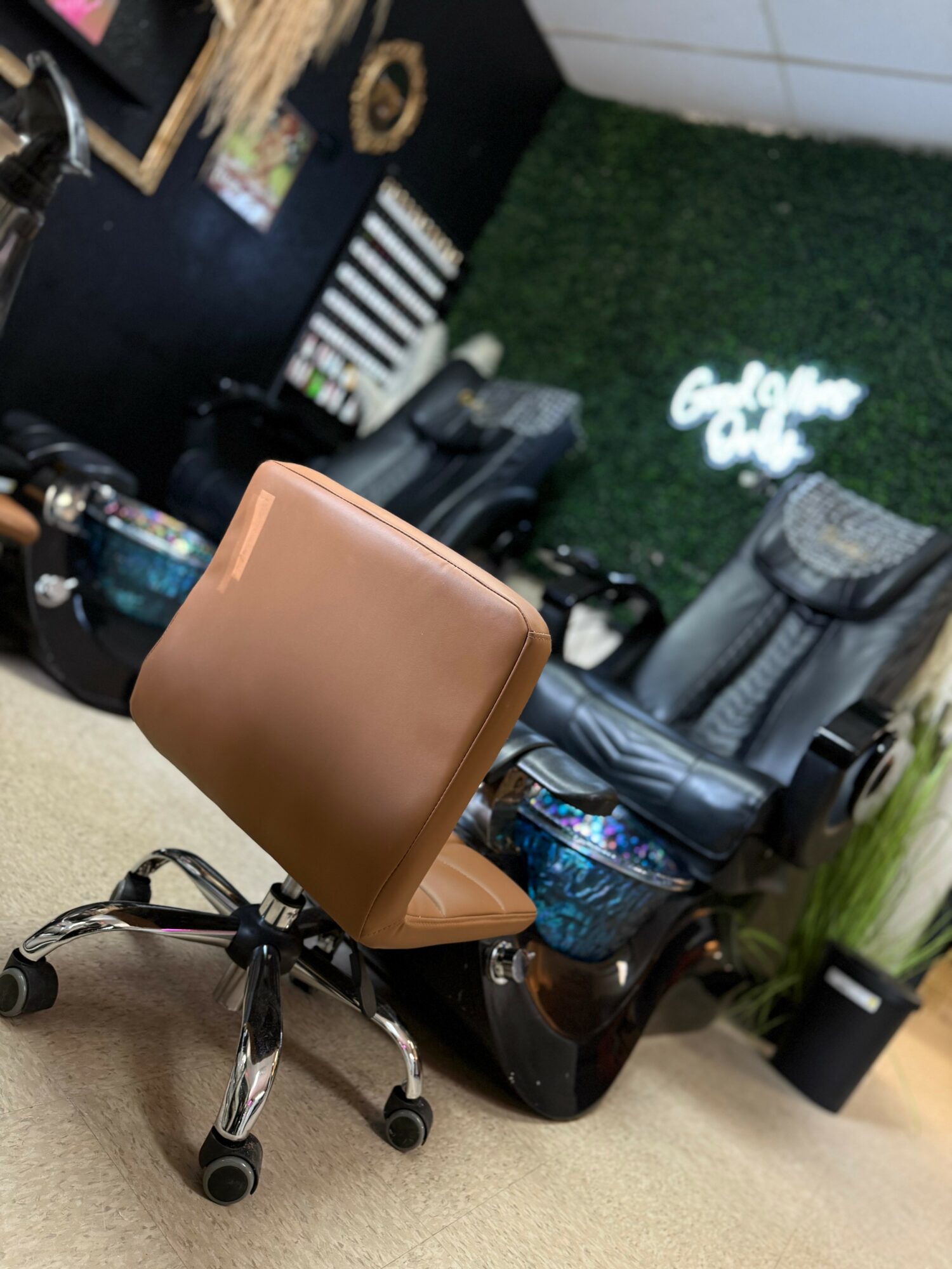 Office chair with brown seat and backrest, on wheels, in a room with black and green decor, and a neon sign.