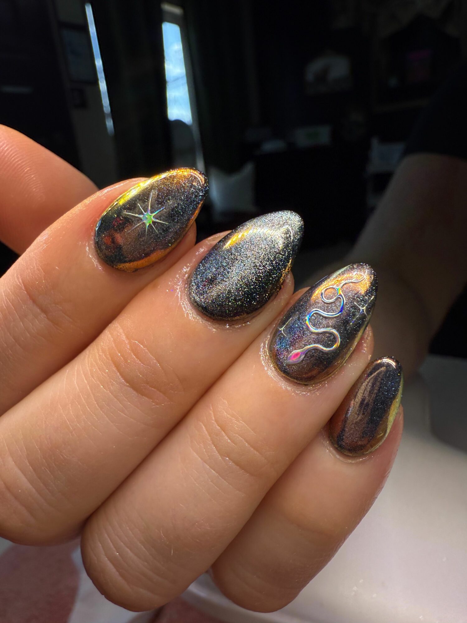 Close-up of a hand with decorated nails featuring galaxy and star designs, with a dark background.