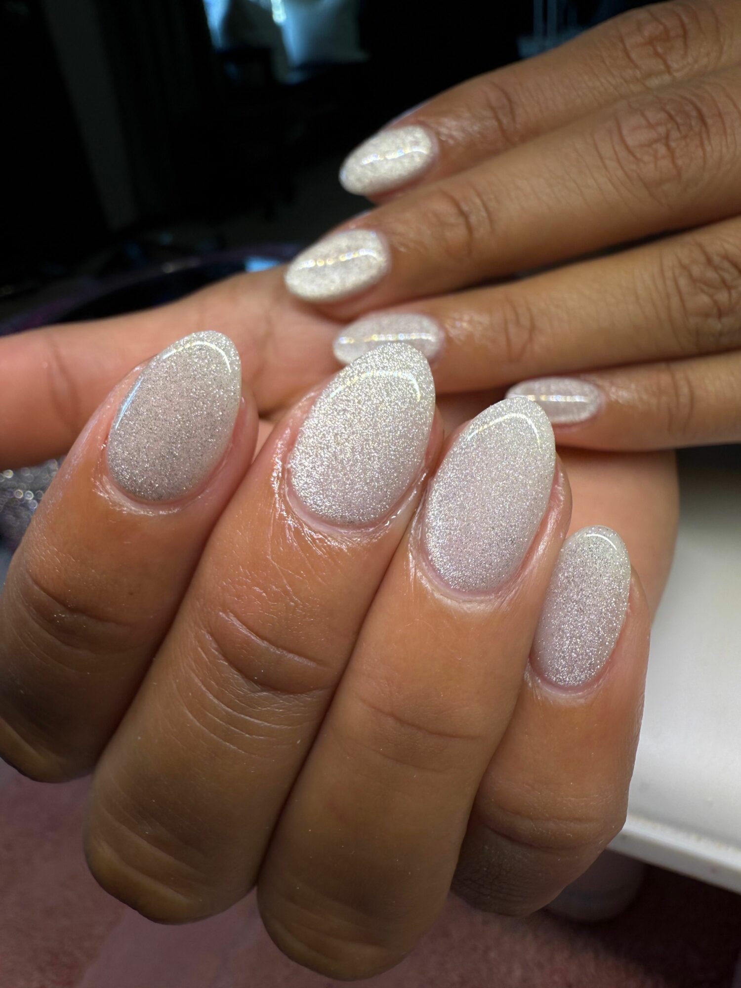 Close-up of hands with glittery, silver nail polish on fingernails, showing well-manicured nails and skin.