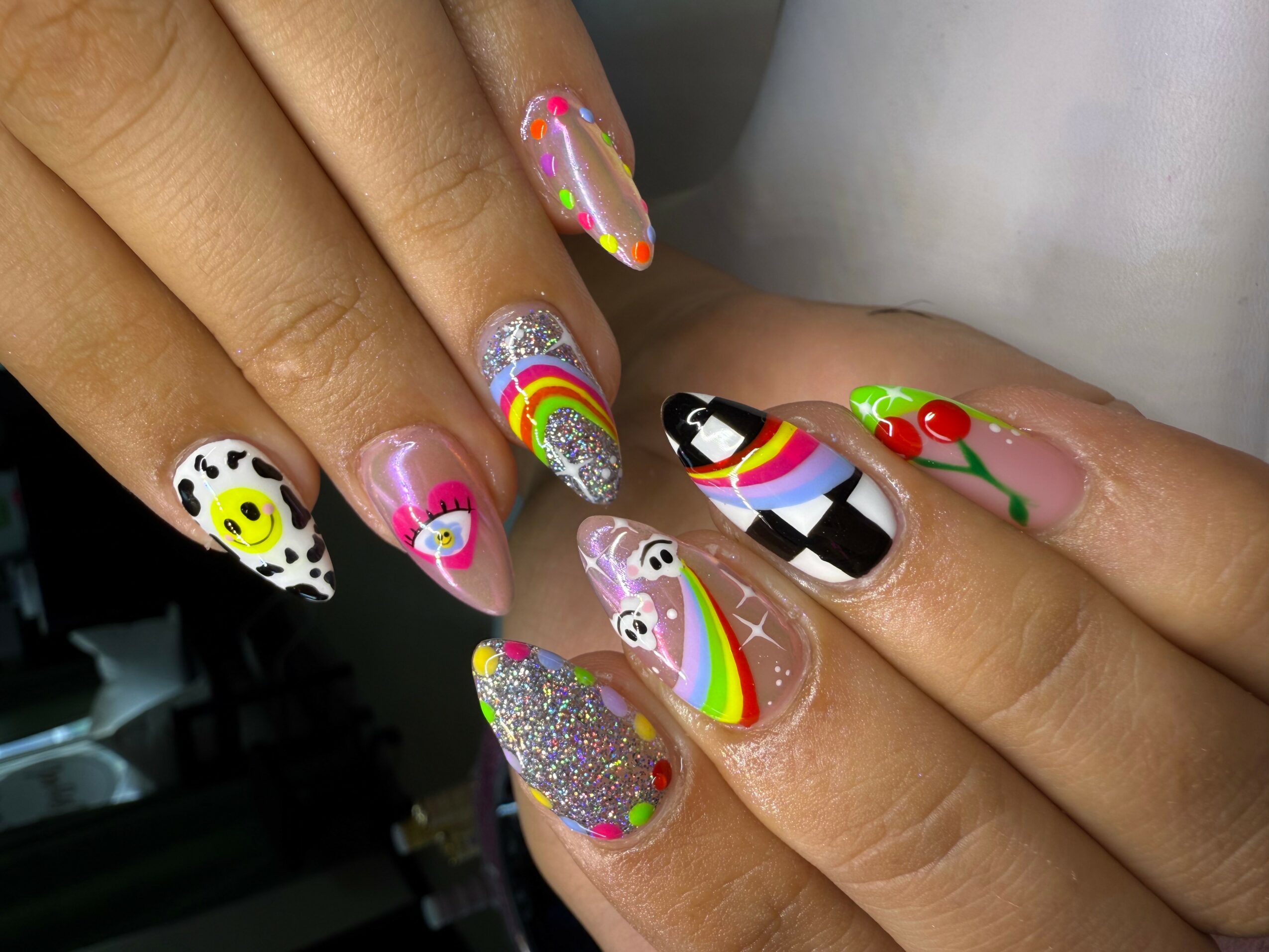 Close-up of hands with colorful, decorated nails featuring various patterns and glitter, held together with fingers slightly apart.