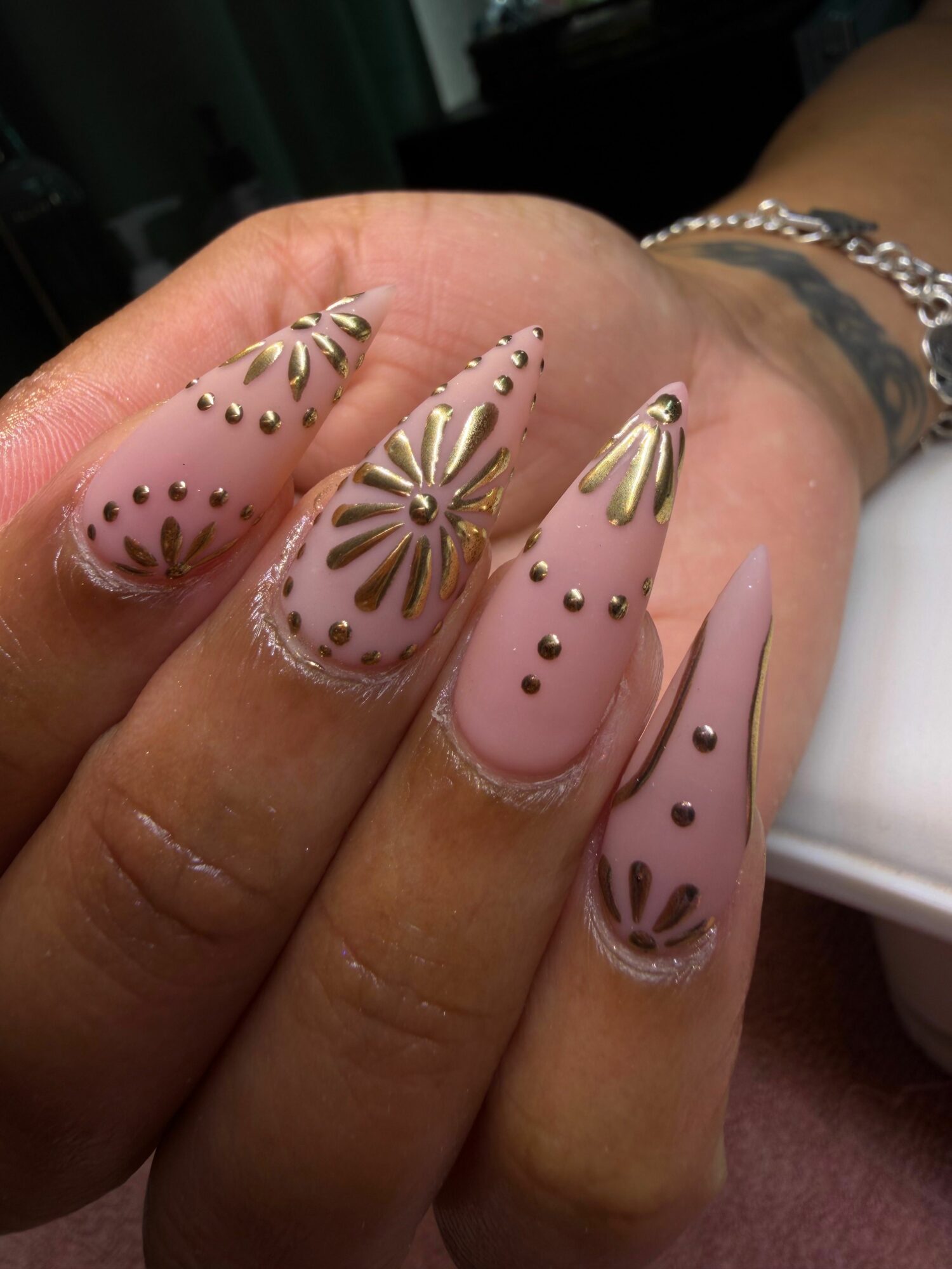 Close-up of manicured nails with pink polish and gold floral designs, on a person's hand.