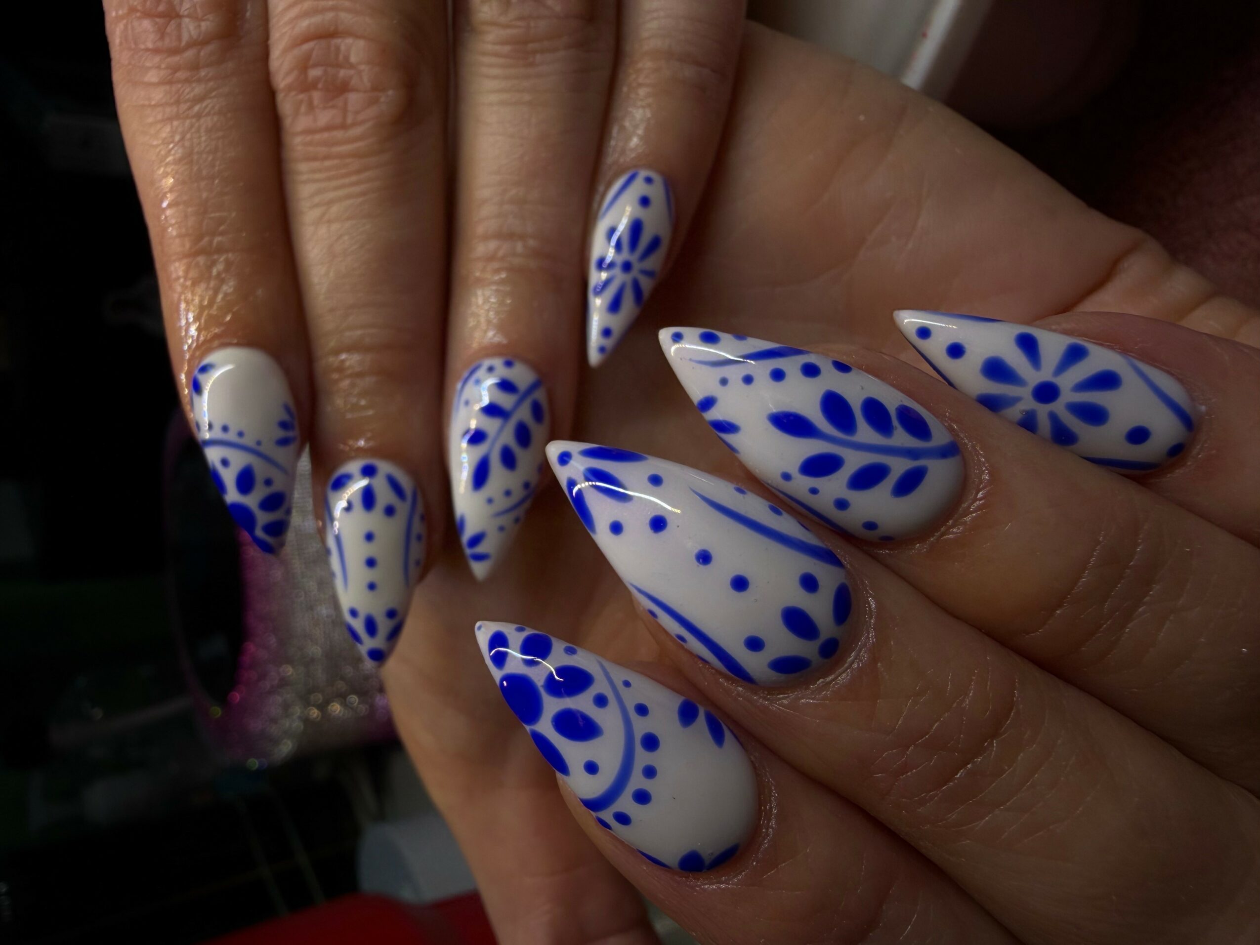 Hand with long, pointed nails painted with white and blue floral patterns.