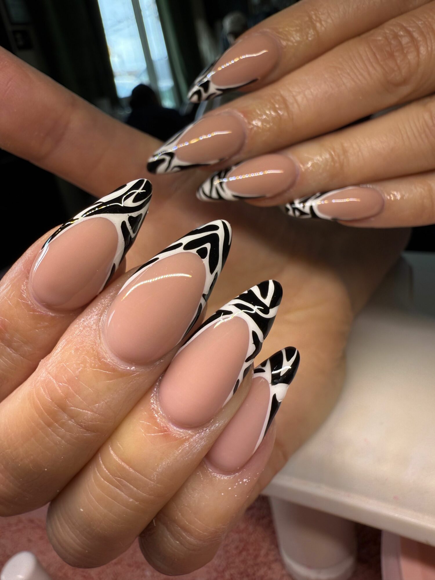 Close-up of hands with long, almond-shaped nails featuring black and white abstract designs on tips.