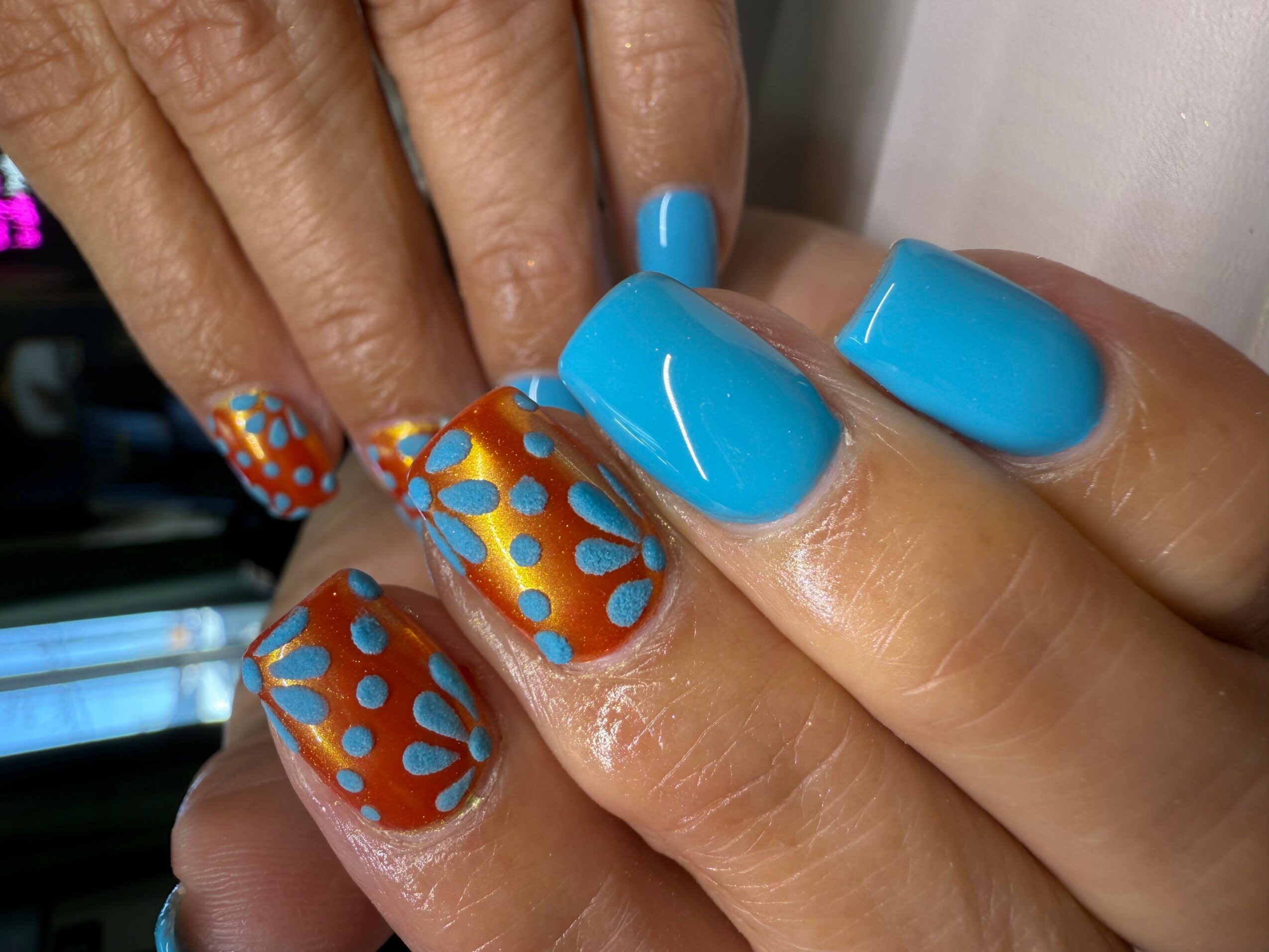 Close-up of hands with blue and decorated orange nail polish, featuring polka dot patterns.