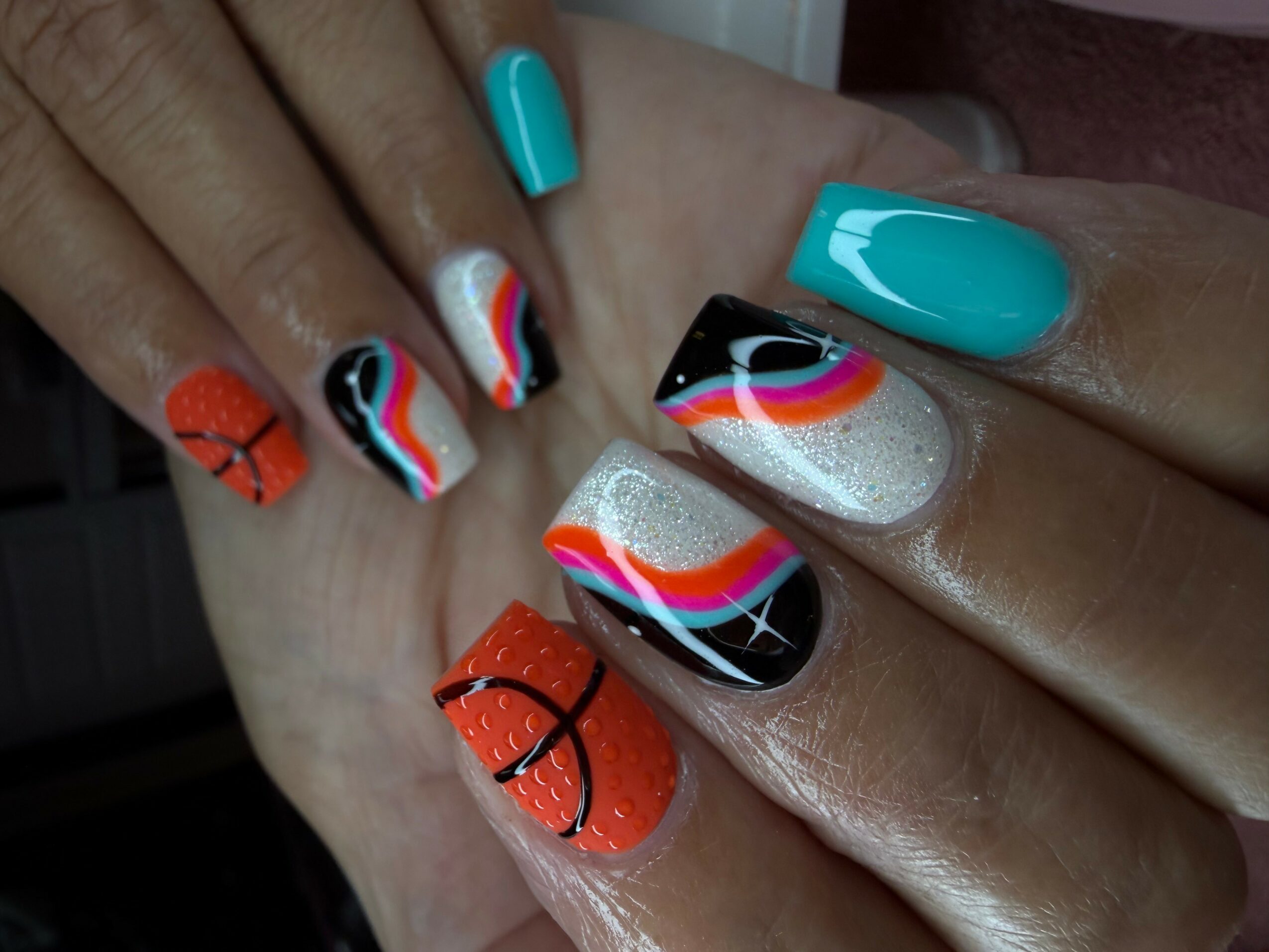 Two hands with colorful, patterned nail art, including orange, black, white, rainbow, and turquoise designs, with a glittery accent.