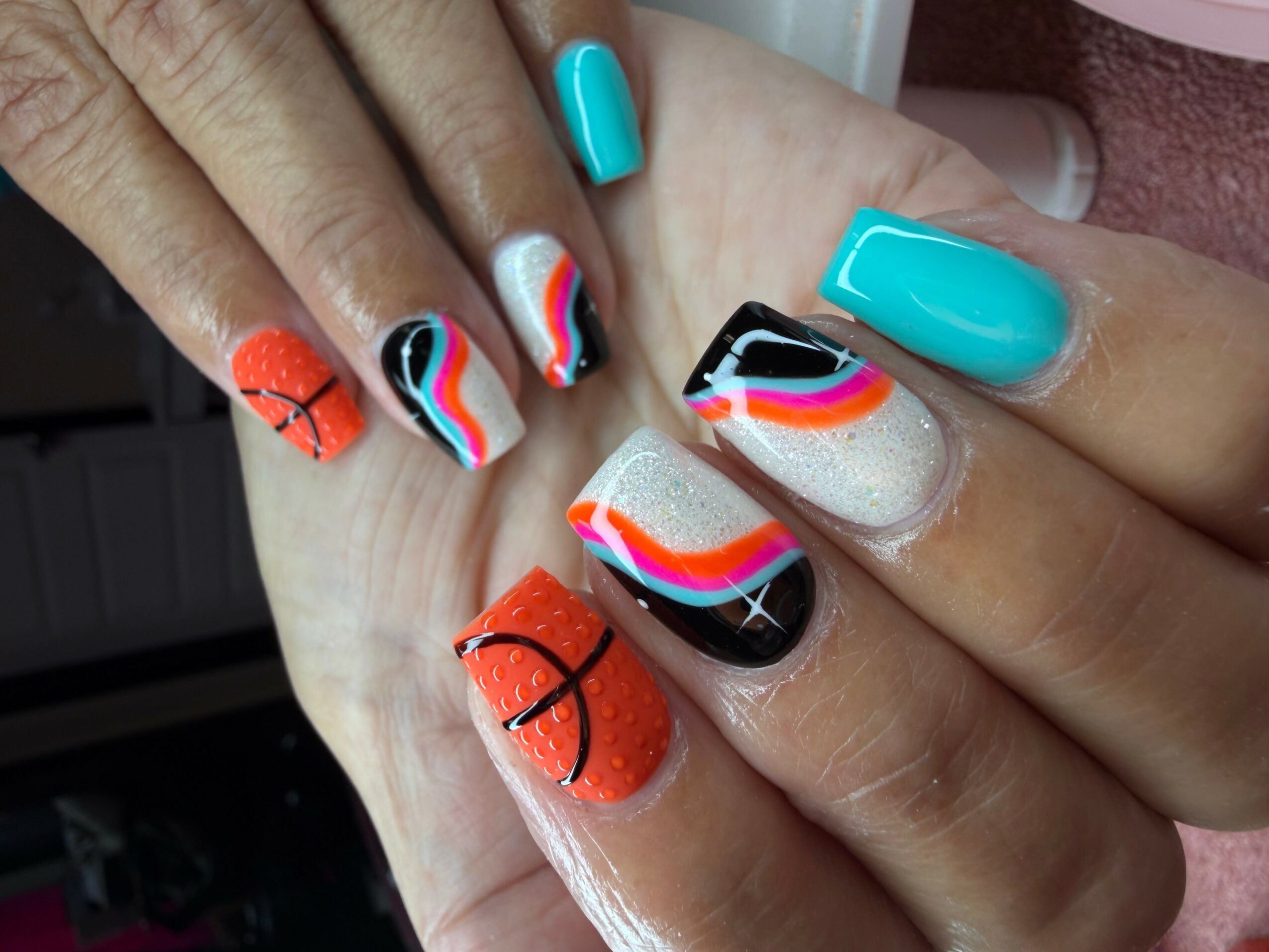 Close-up of hands with colorful rainbow and black nail art designs, including orange, blue, and white colors, and black lines.