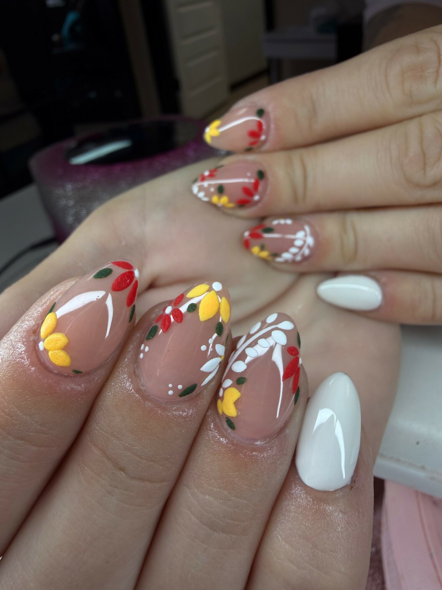 Close-up of hands with colorful floral and white nail art, some nails with clear polish, background blurred.