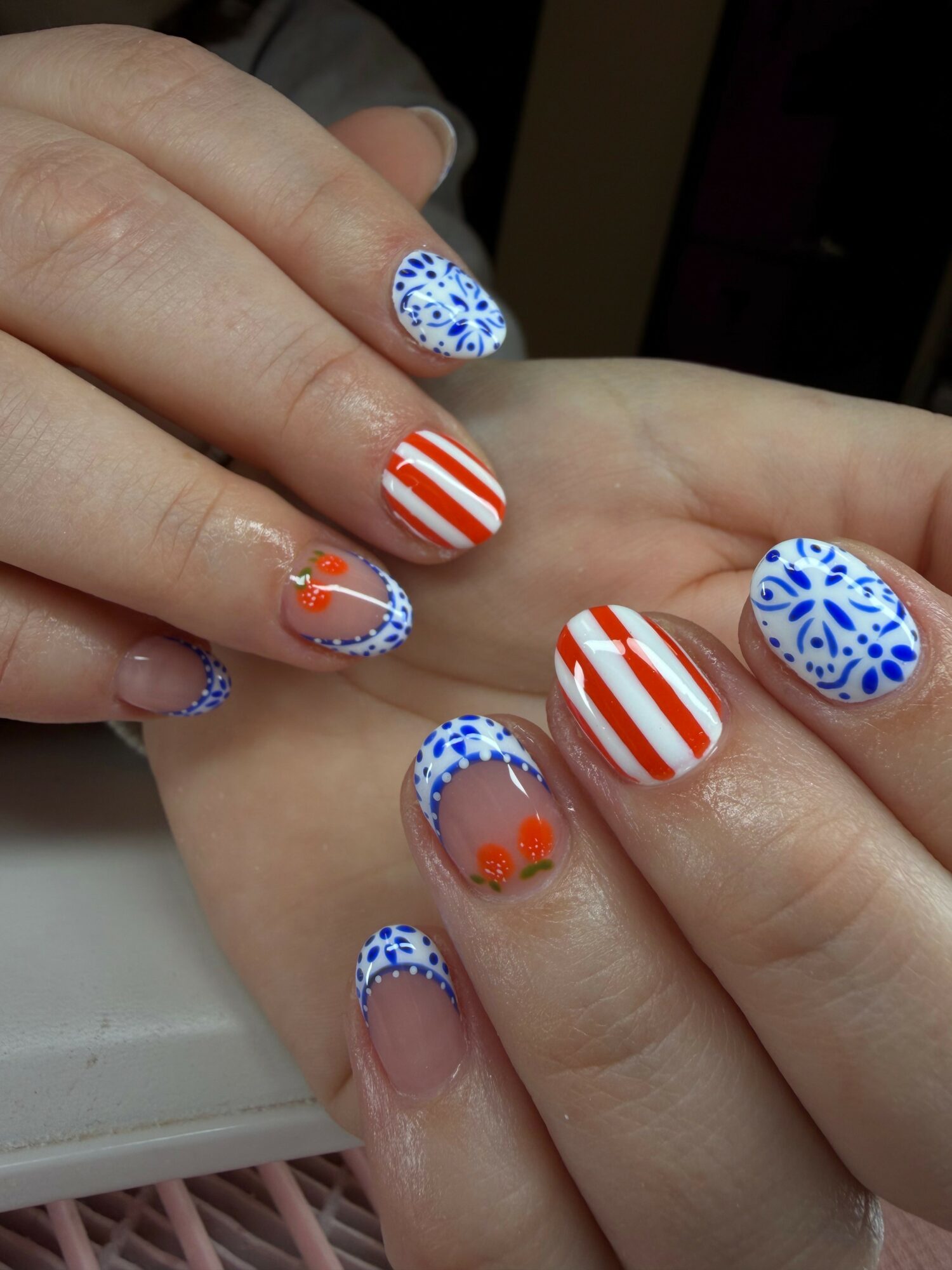 Hands with patriotic nail art featuring red, white, and blue patterns, including stripes and floral designs, on short nails.