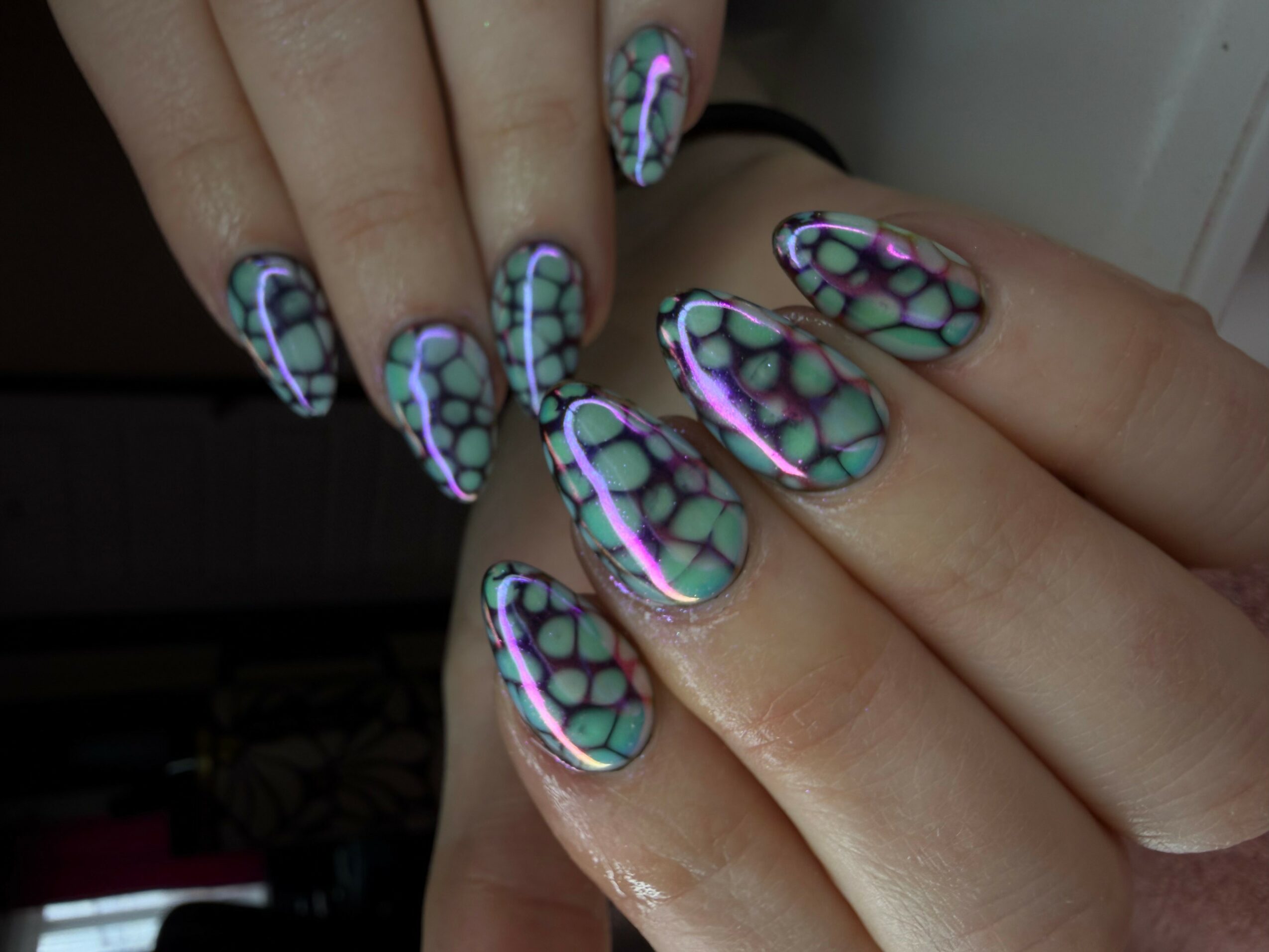 Close-up of hands with colorful, patterned nail art featuring a honeycomb design and iridescent accents.