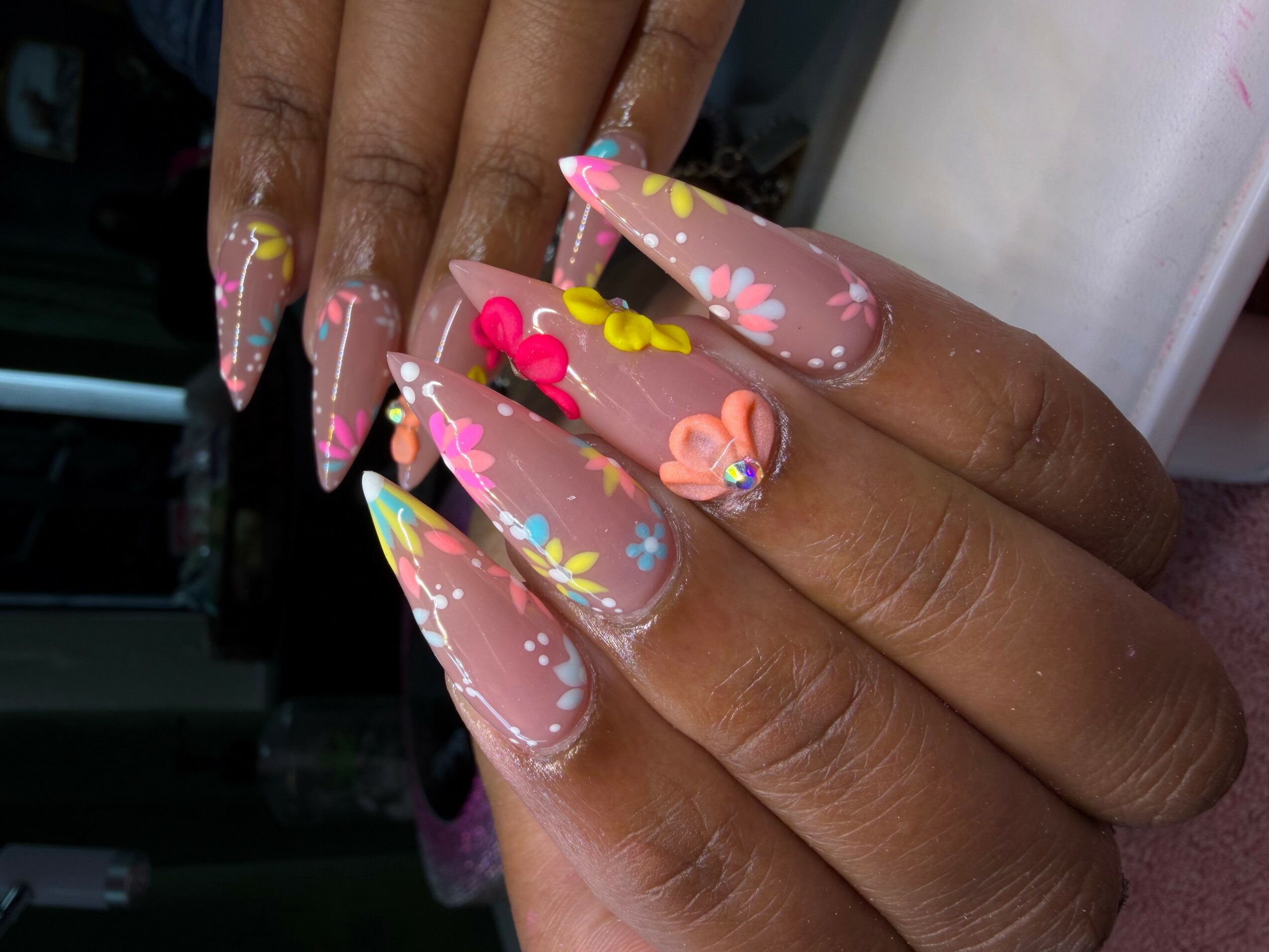 Close-up of long, decorated nails with pink, yellow, and blue floral designs and white accents.