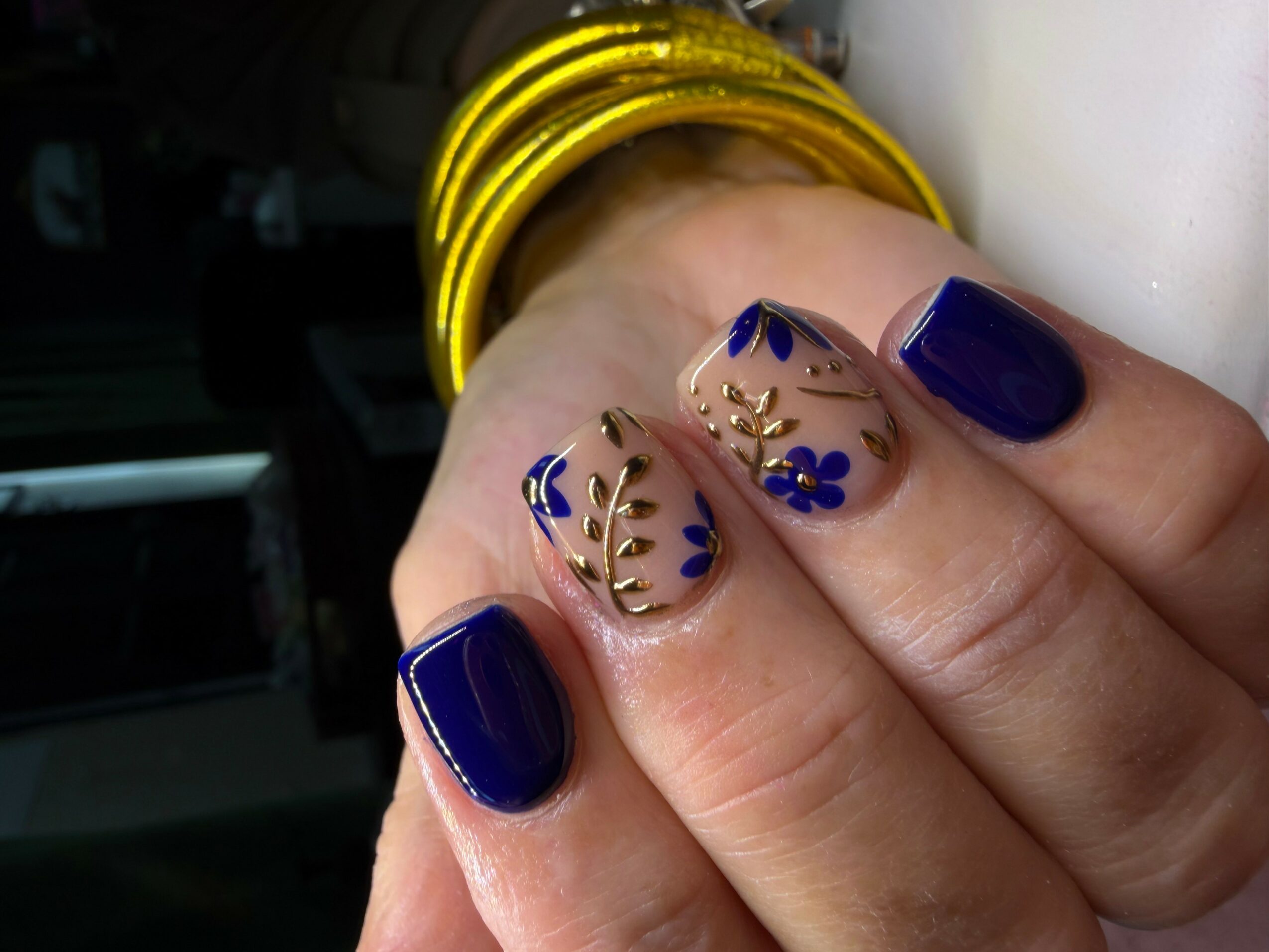 Close-up of a hand with decorated nails, some painted dark blue and others with floral designs and gold accents.