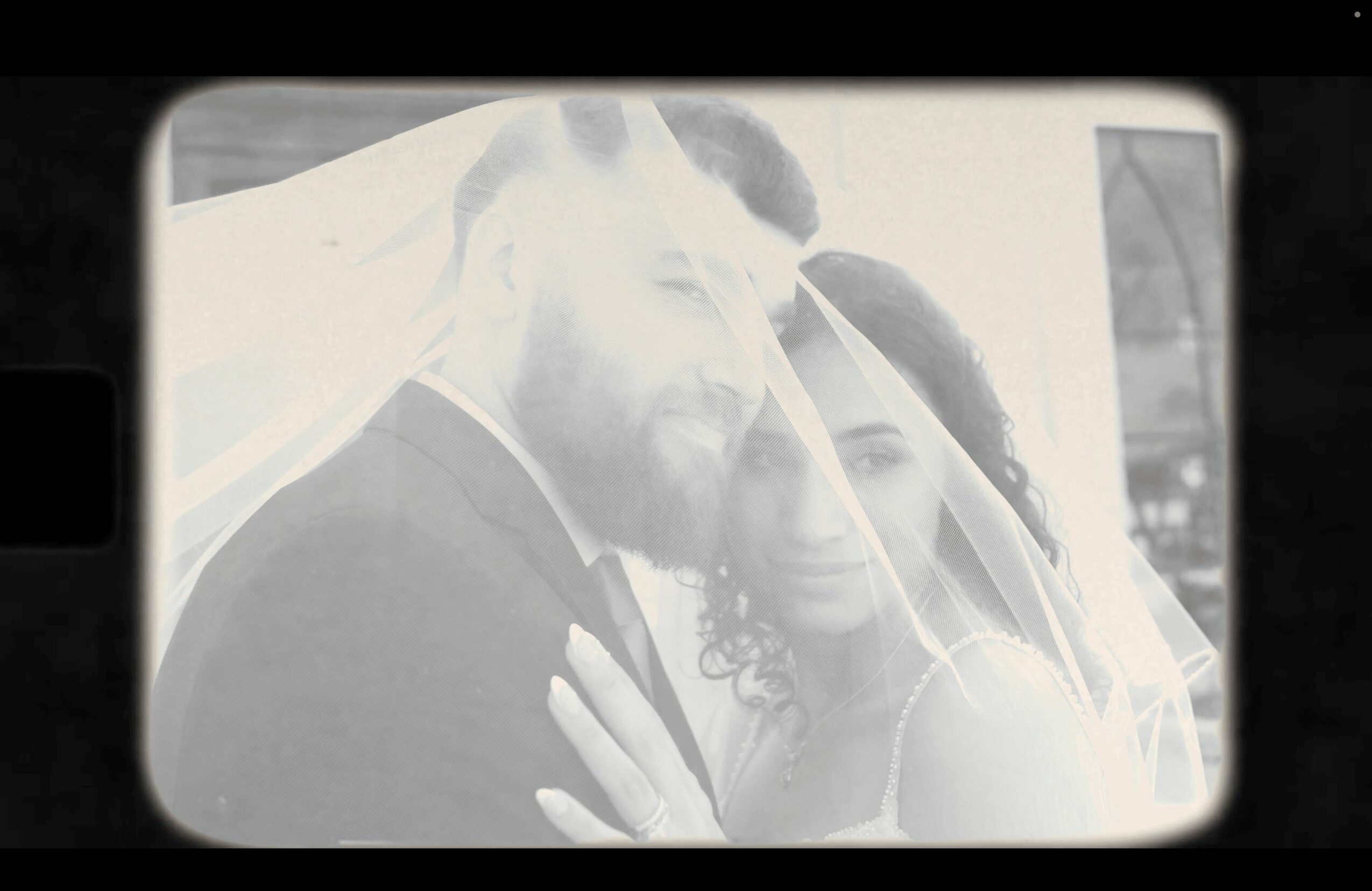 A couple under a veil, close together, with a city background, in black and white.