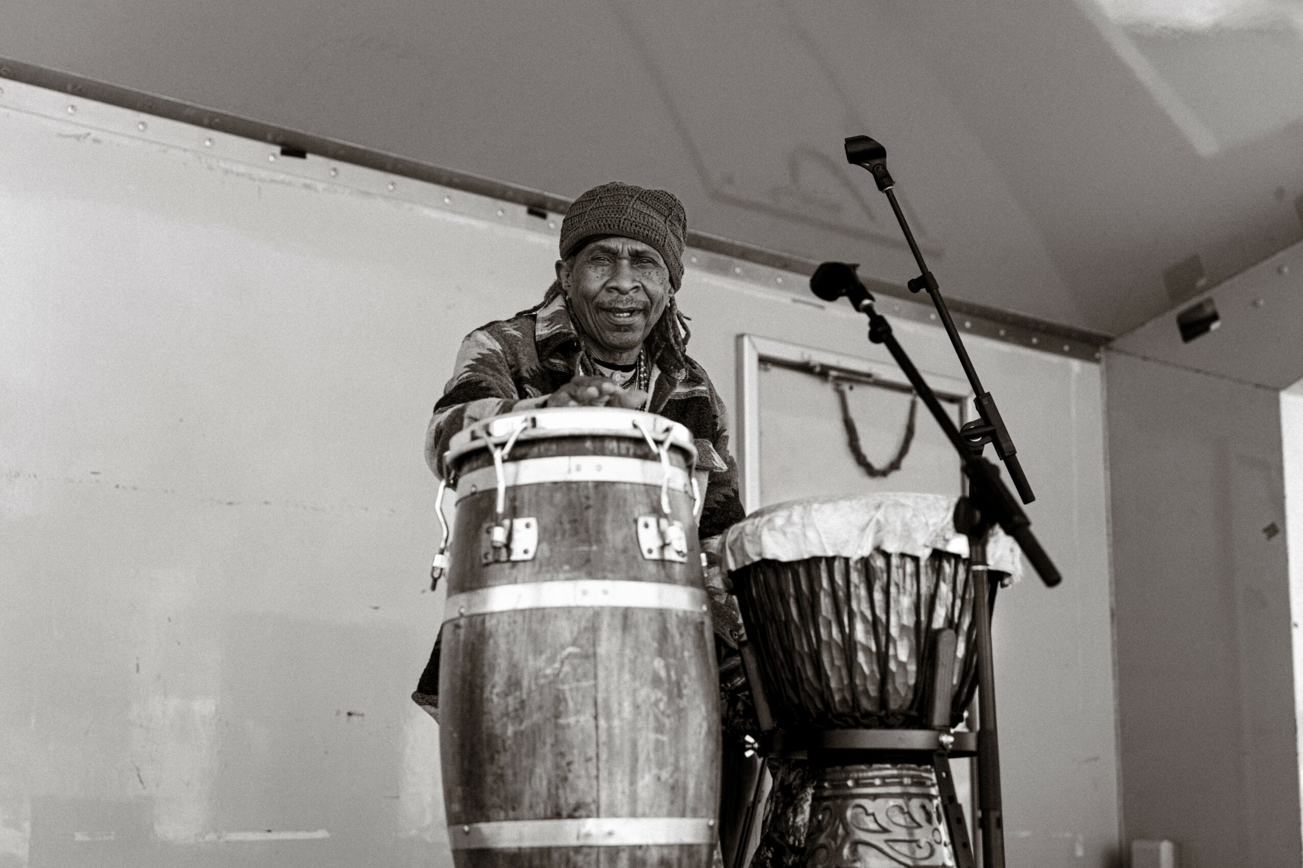 A person standing behind drums with microphones in front, in a performance setting.