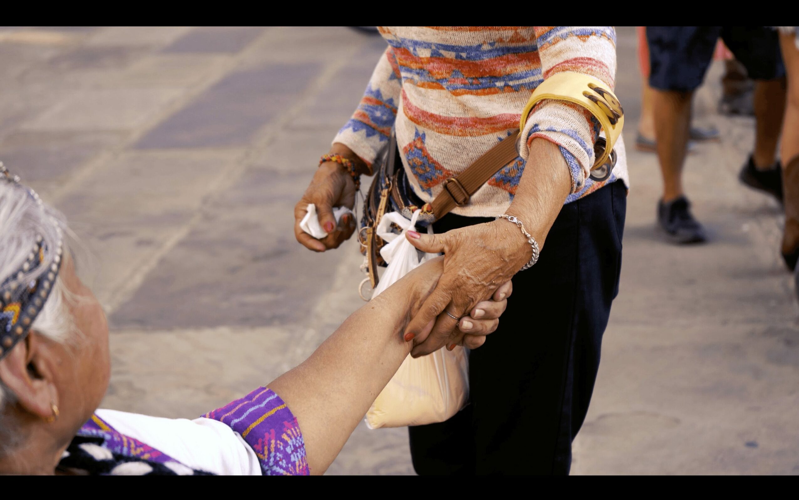 Person handing money to another person on a street, with people walking in the background.