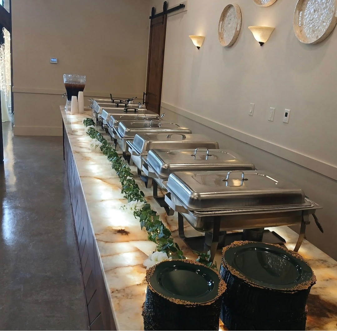 Buffet table with chafing dishes, green garland, and two black baskets in a room with wall decor and wall sconces.