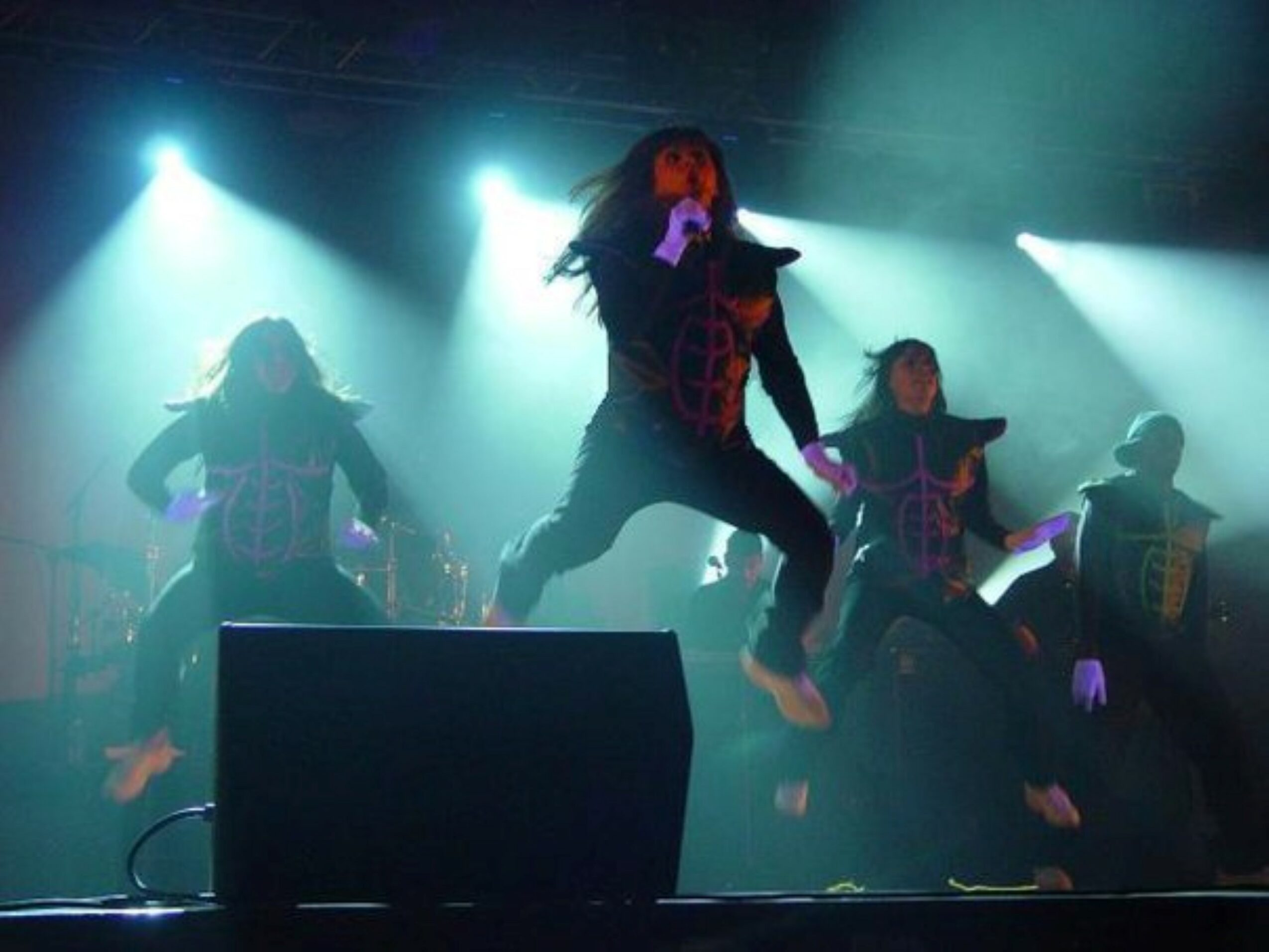 Group of performers dancing on stage with bright lights and fog effects, mid-air jump, energetic movement, stage equipment visible