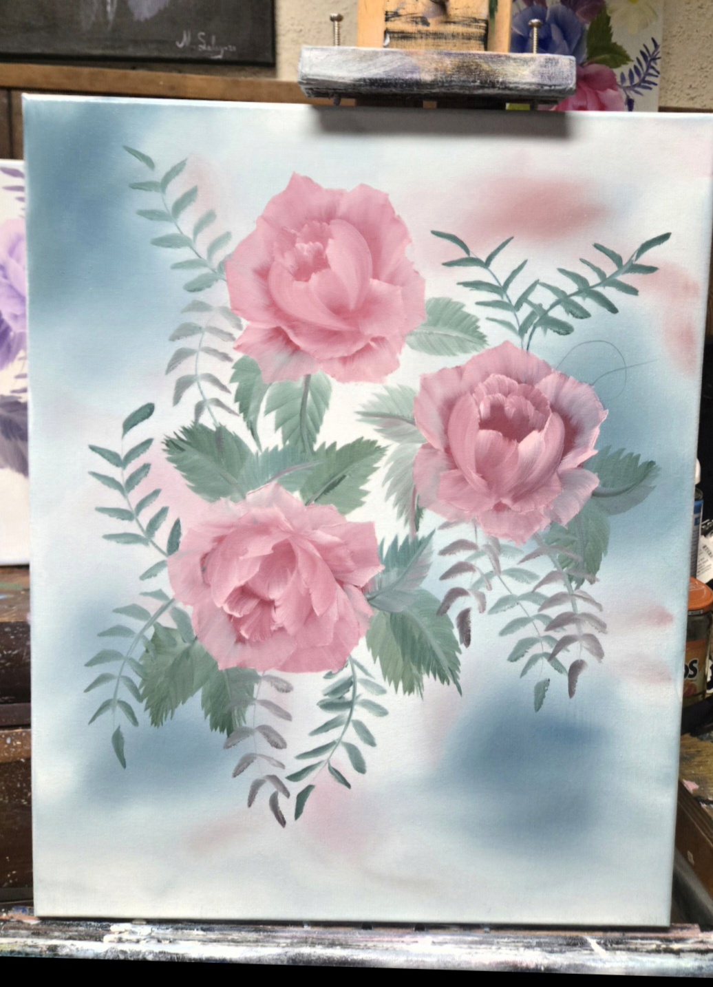 Painting of three pink peonies with green leaves and fern-like foliage on a light blue background.