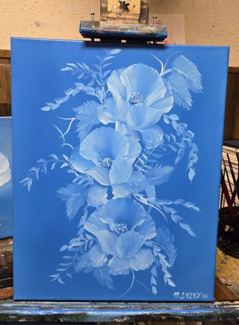 Blue painting of three large flowers with leaves, signed in the bottom right corner.