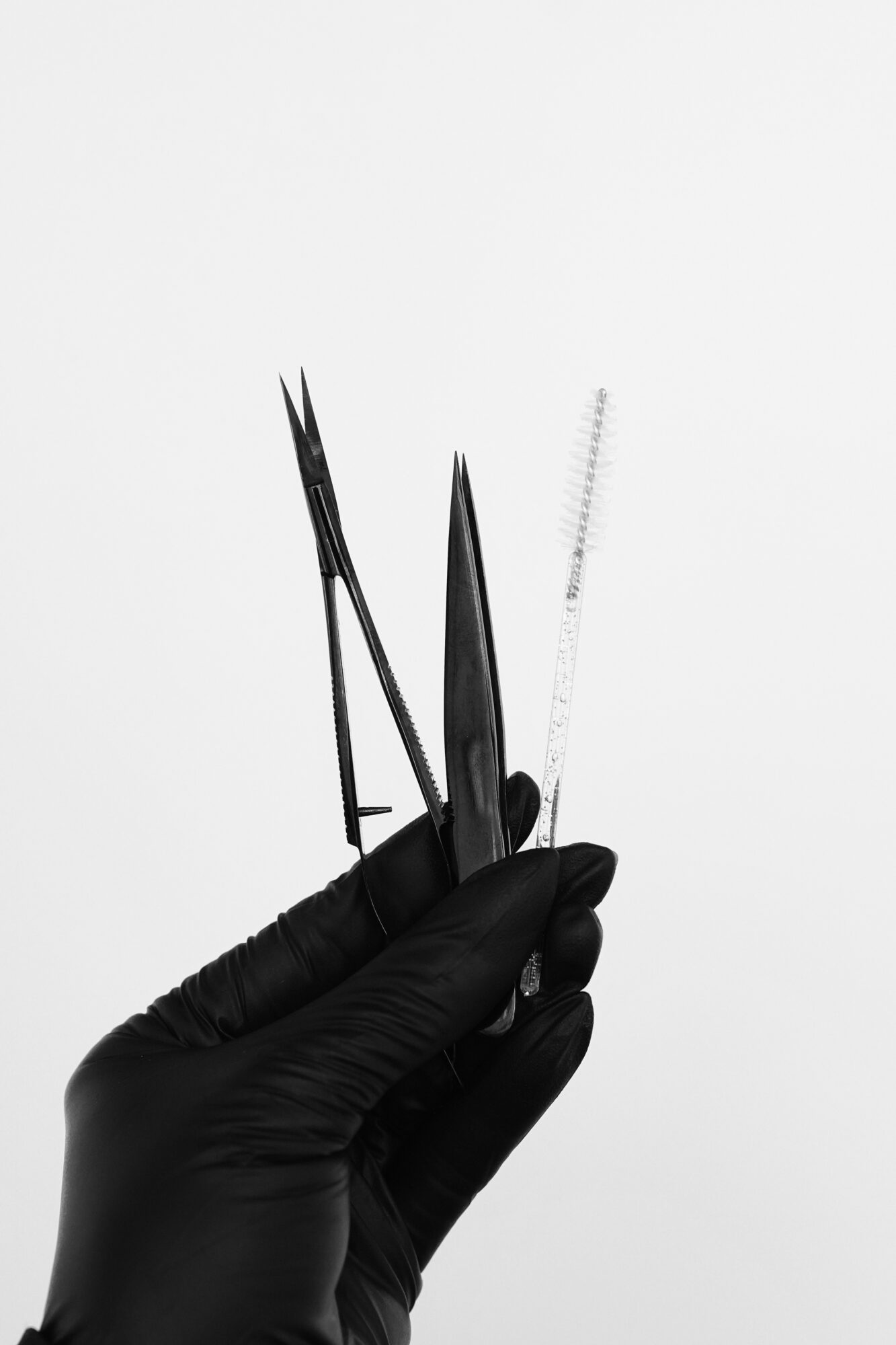 Hand wearing a black glove holding three precision tools against a plain background.