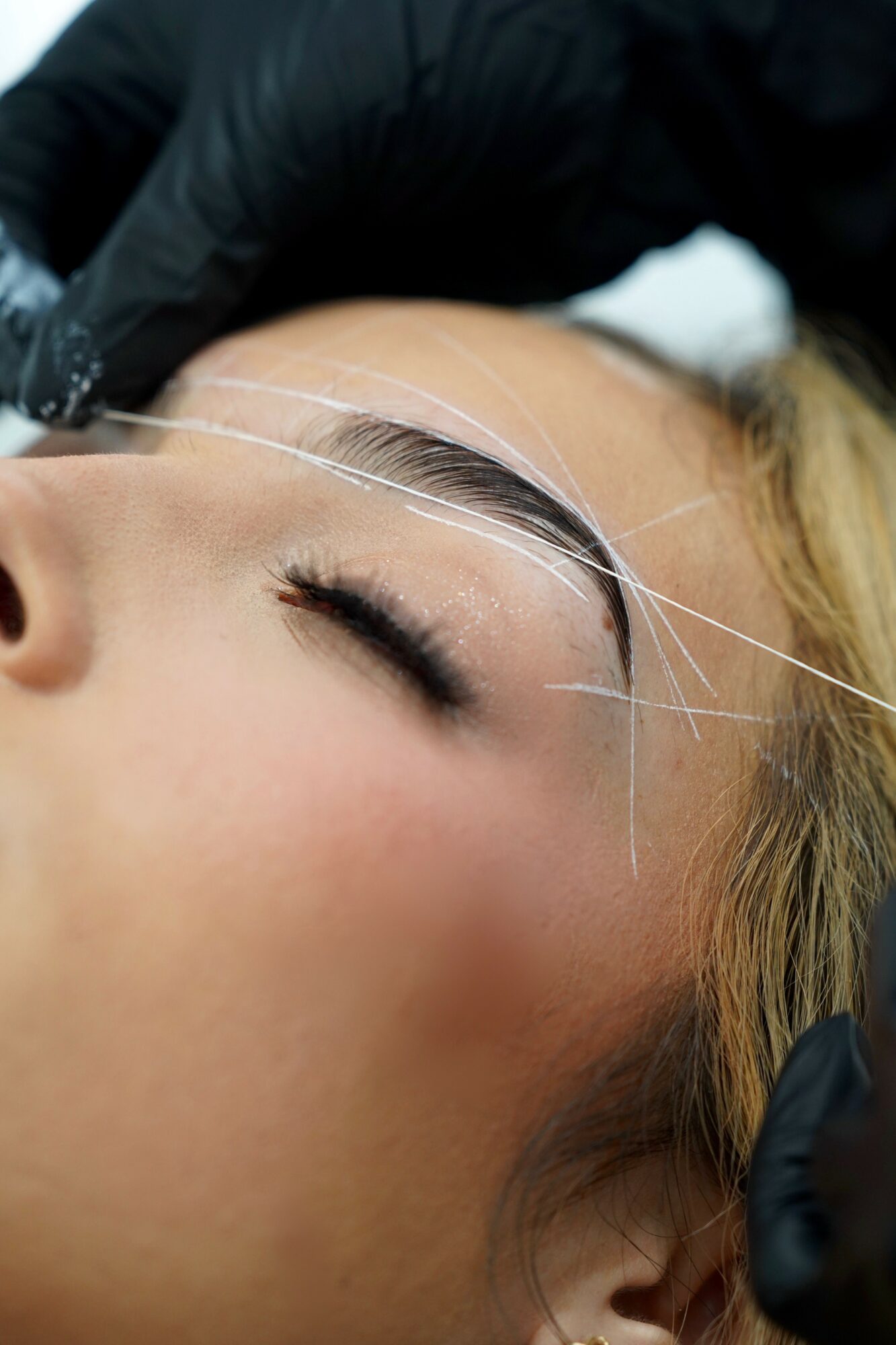Close-up of a woman receiving eyelash extension treatment, with a technician applying extensions near her closed eye.