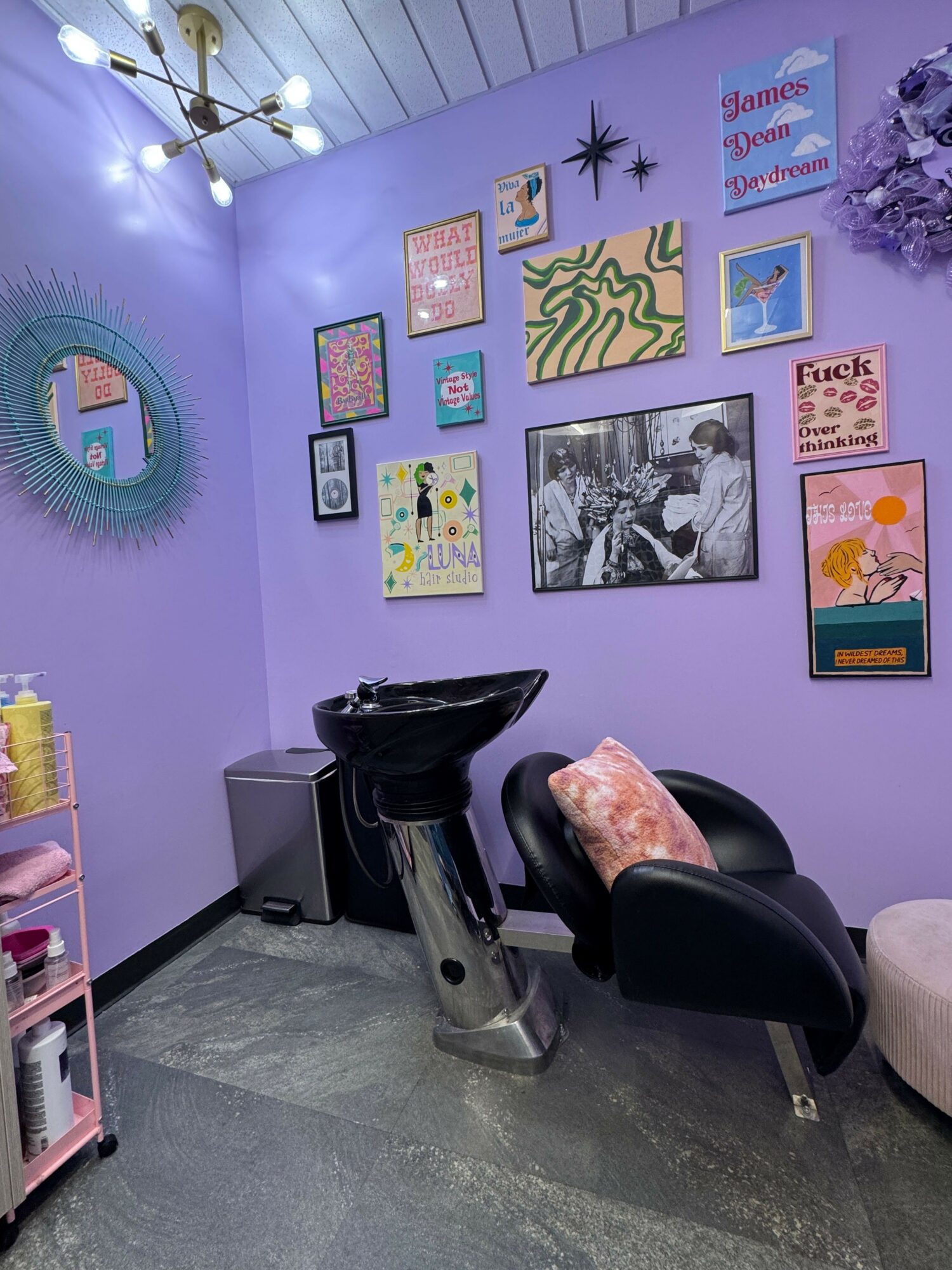 Purple wall with framed artwork, a black chair, and a small table with a pink item, in a modern room.