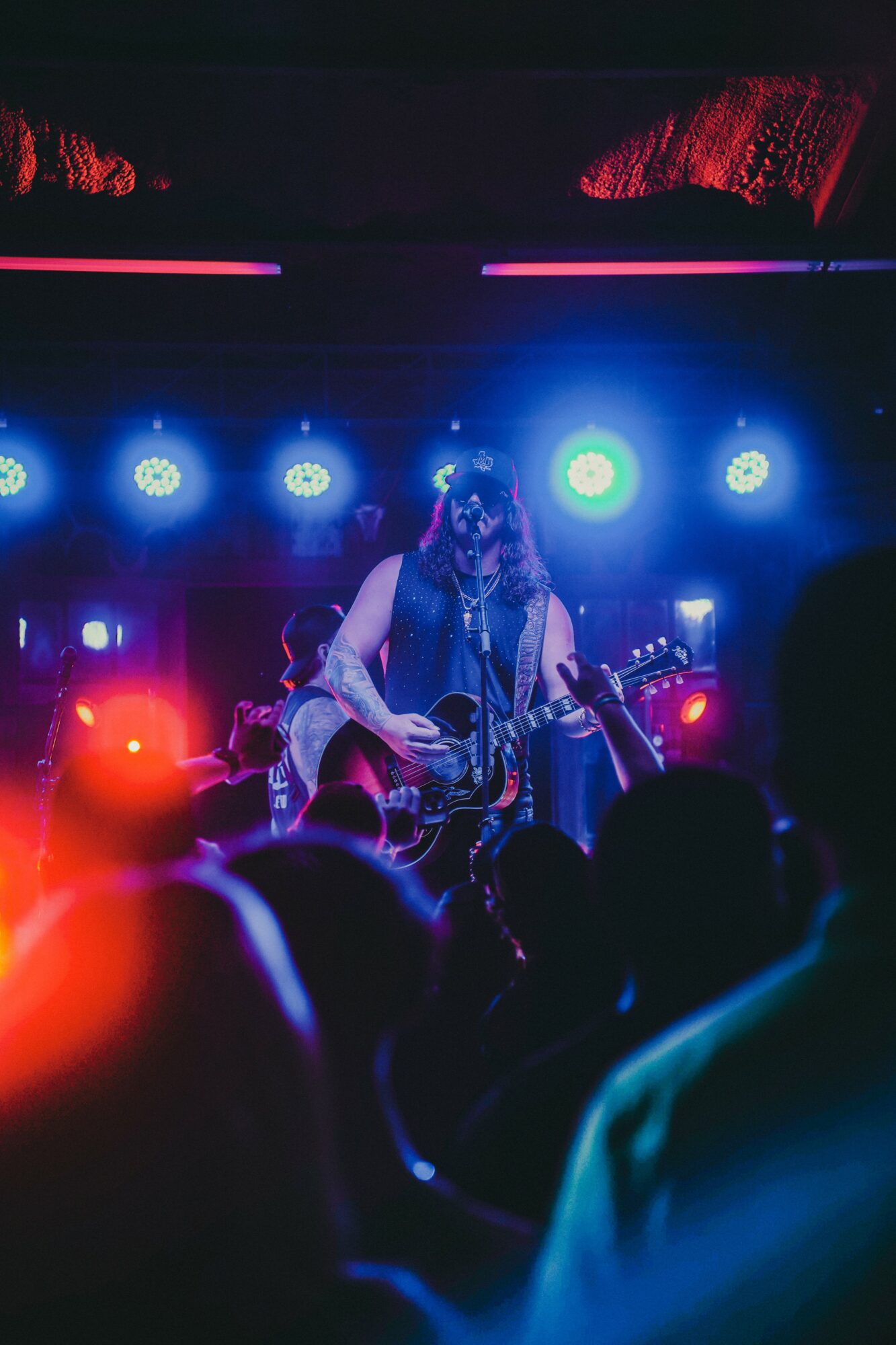 Musician playing guitar on stage with colorful lights and audience in foreground.