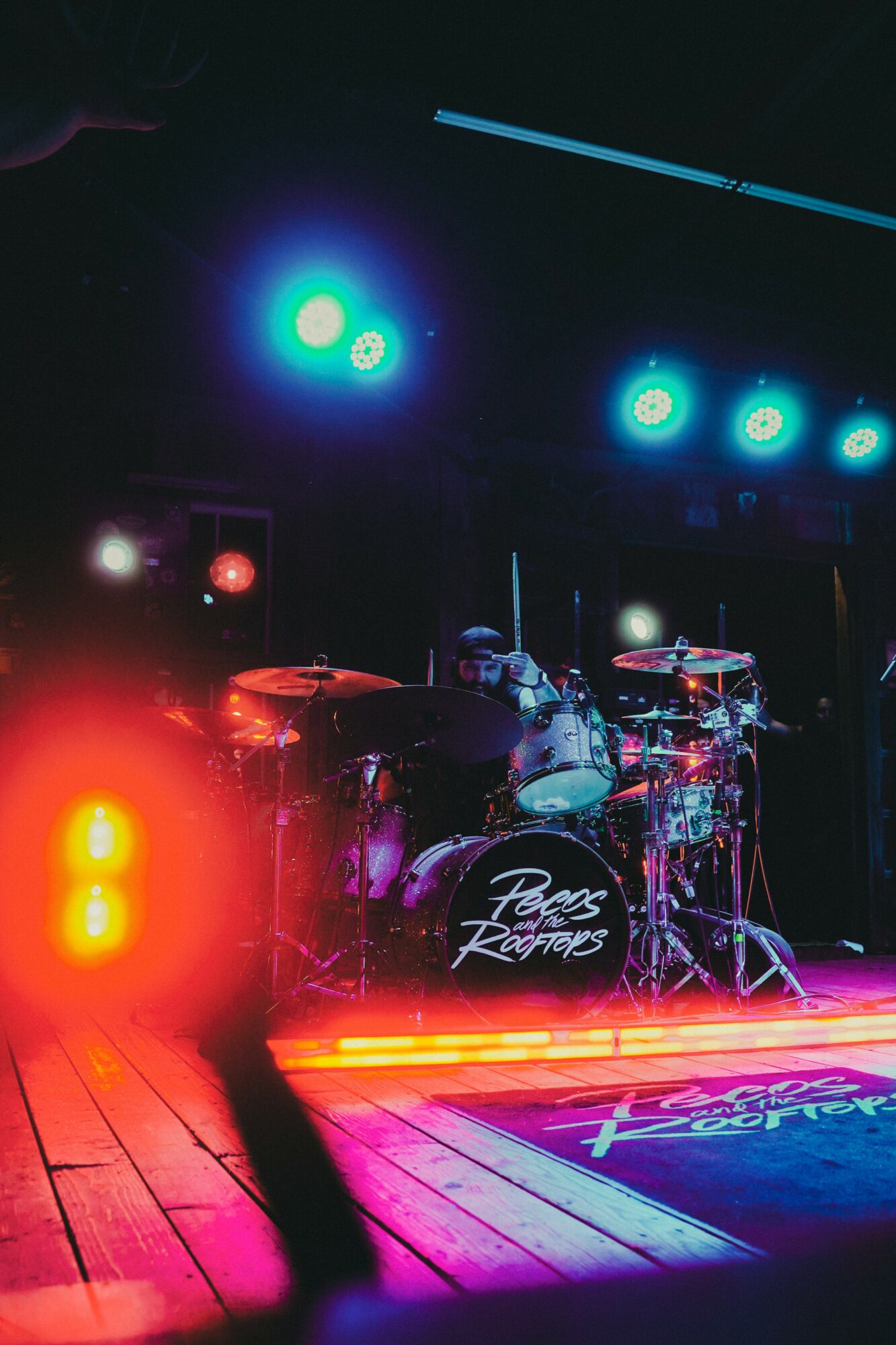 Stage with drum set and colorful lighting, including blue and red lights, on a wooden floor, ready for a performance.