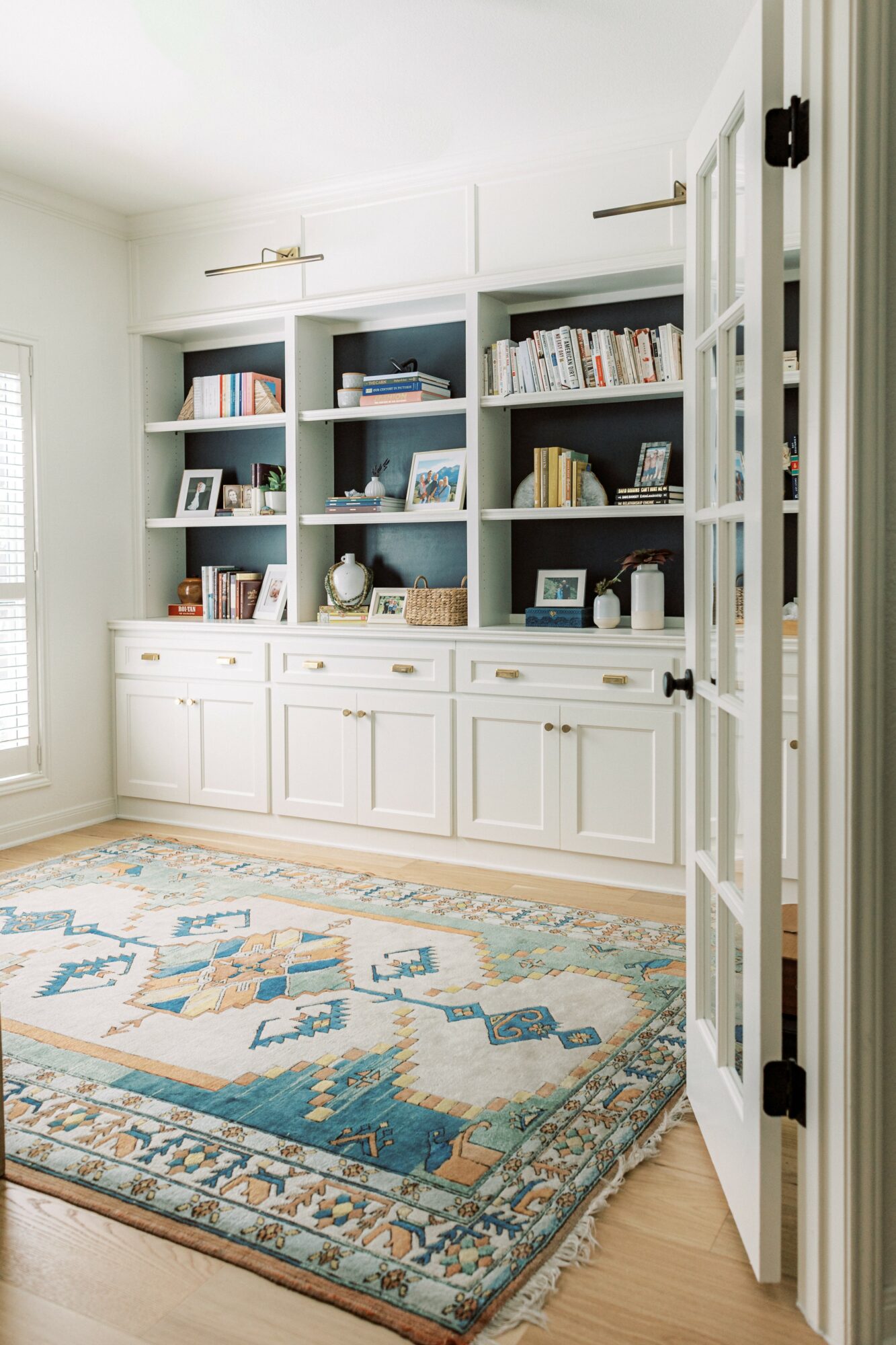 White built-in bookshelf with books and decorative items in a room with a patterned rug and a door frame visible.