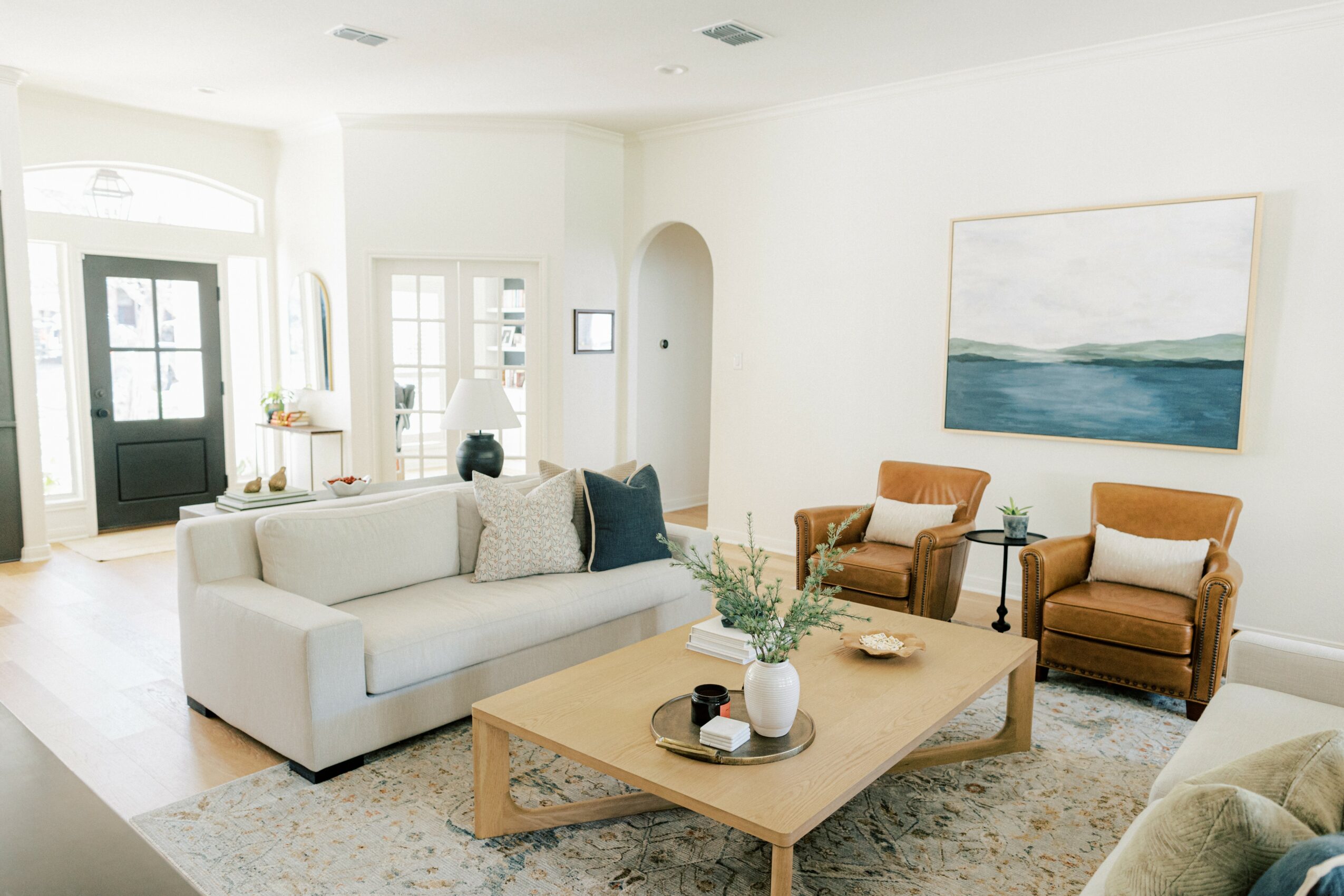 Living room with white sofa, two brown armchairs, a wooden coffee table, and a large abstract painting on the wall.