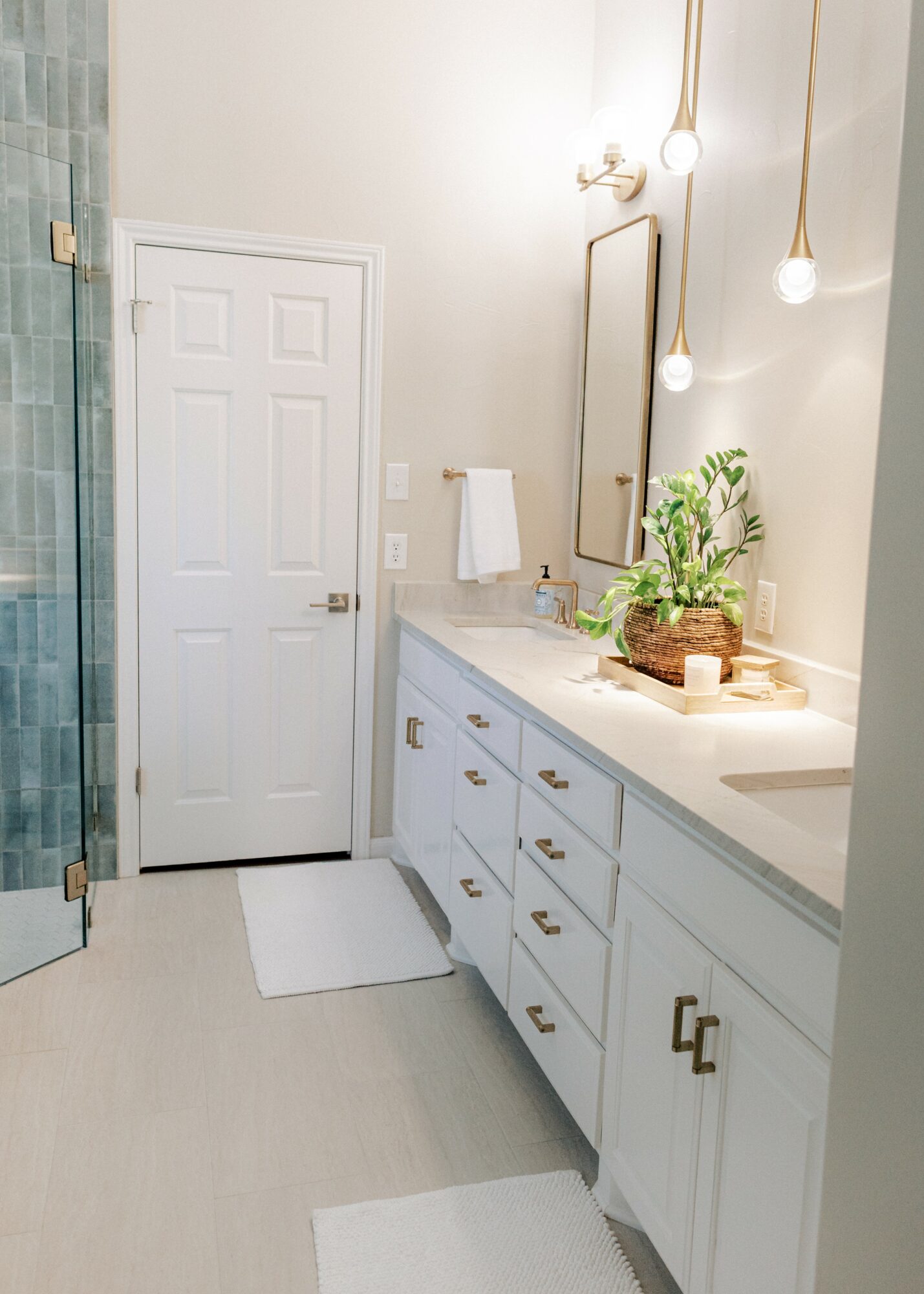 Bathroom with white vanity, mirror, towel, and hanging lights, door, and a plant on the counter.
