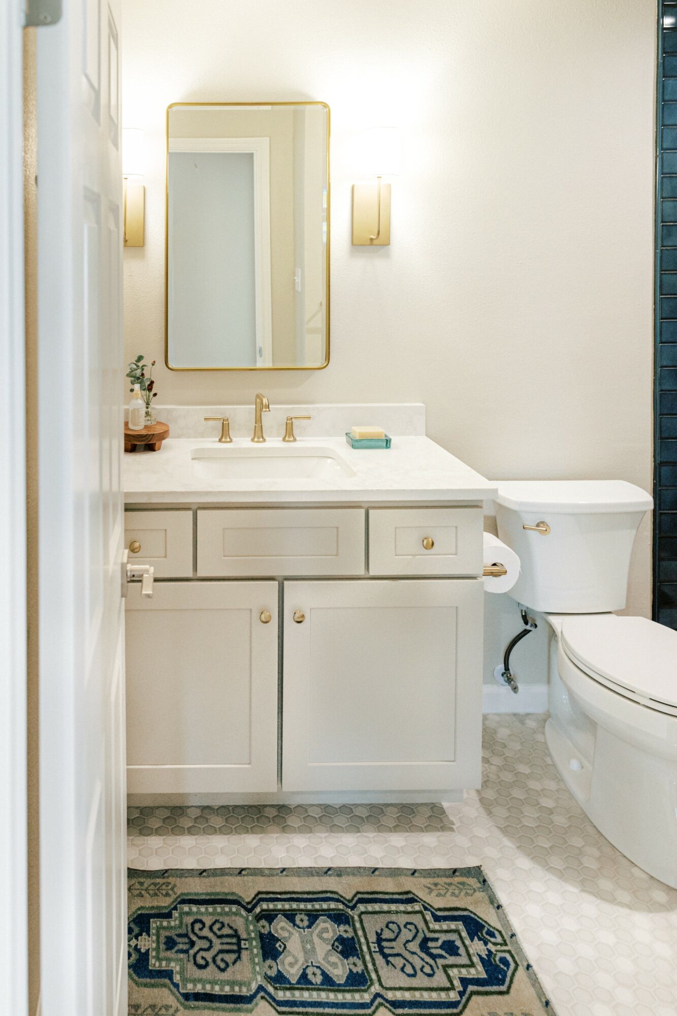 Bathroom vanity with mirror, sink, and cabinet, next to a toilet, with a patterned rug on the floor.