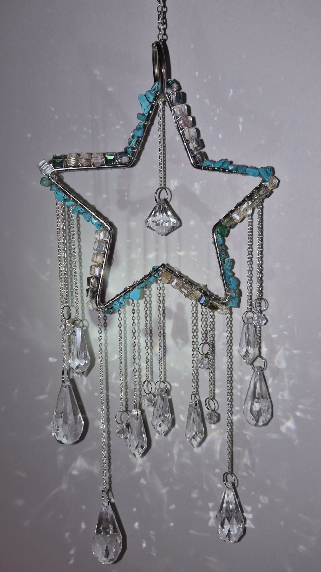 Star-shaped hanging ornament with beads and dangling crystal-like drops, against a plain background.