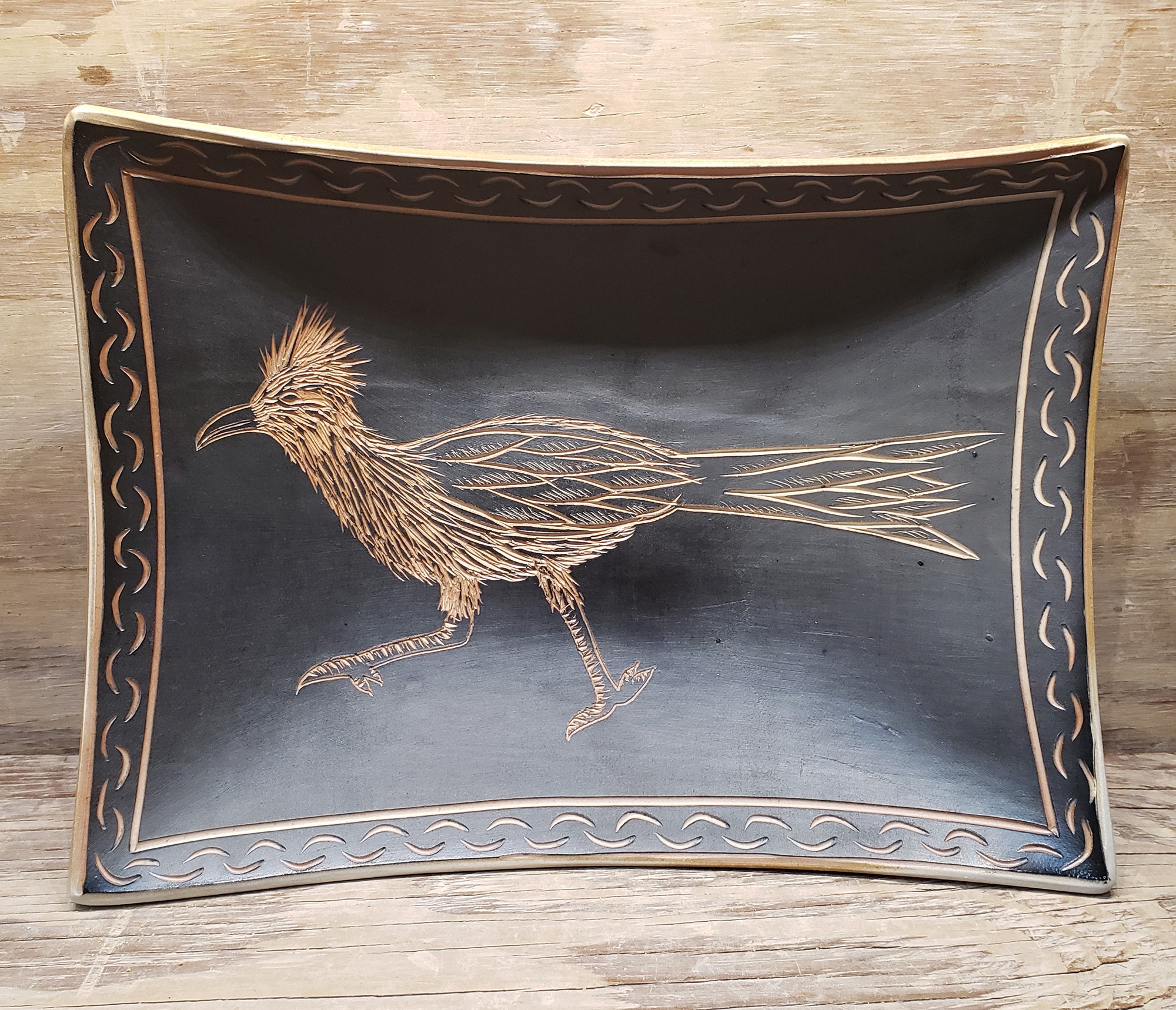 Decorative tray with a bird illustration, curved edges, and a border design, placed on a wooden surface.