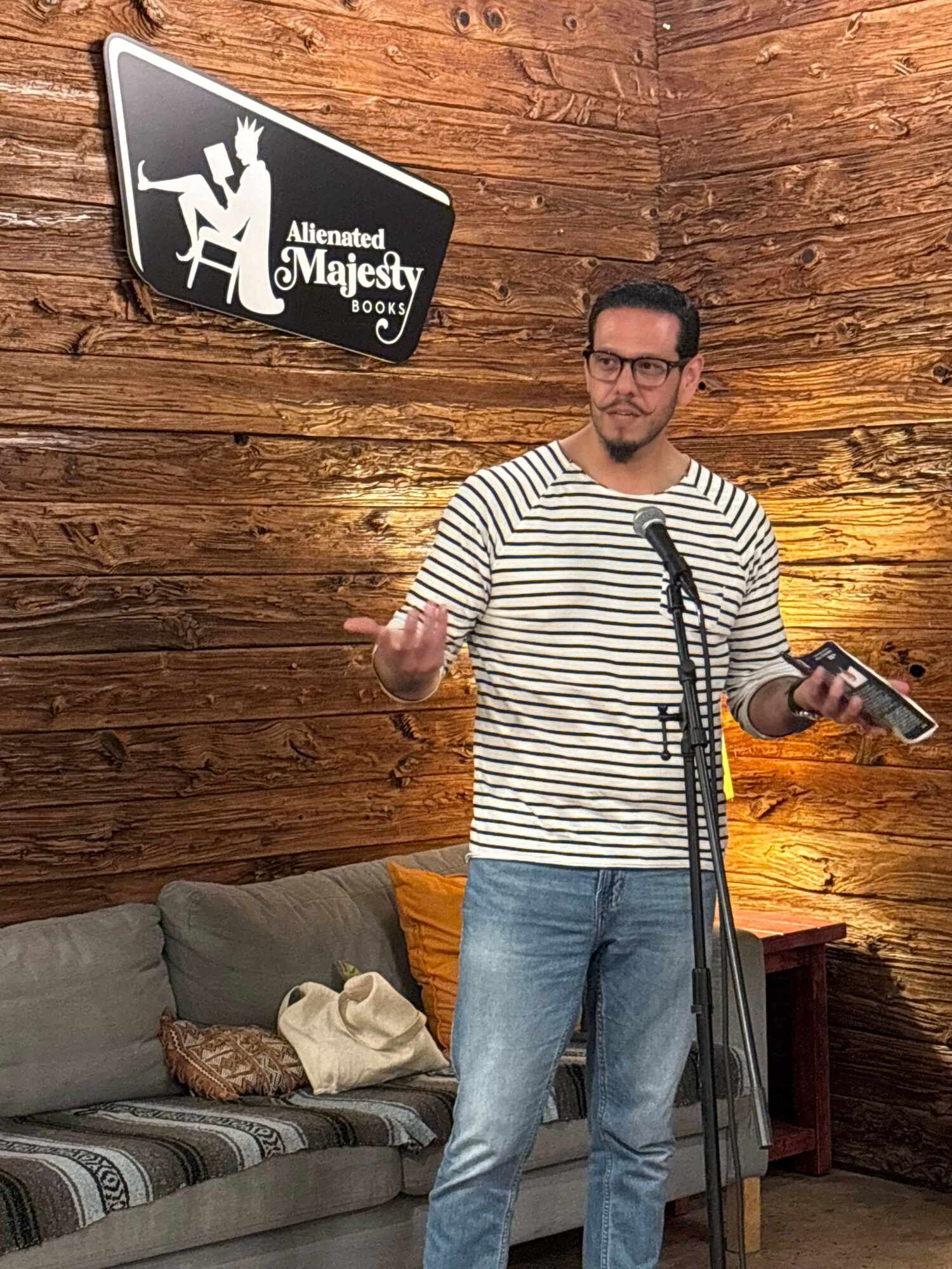 Man with glasses in striped shirt holding a microphone on wooden wall background.