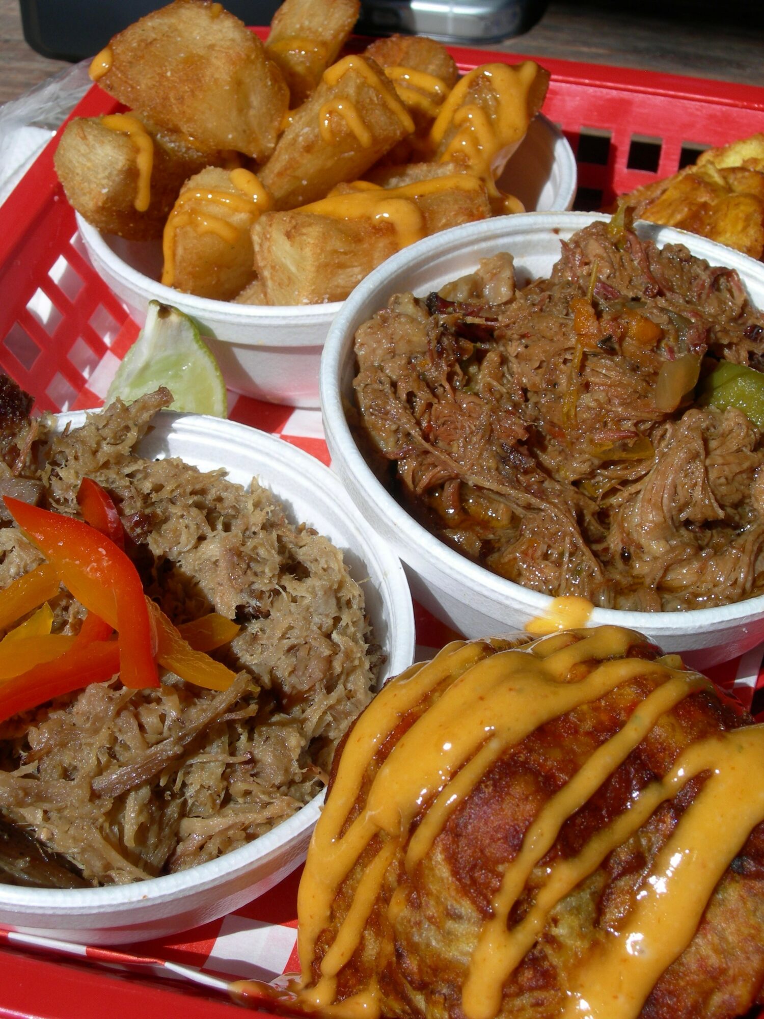 Three bowls of food with fried items, shredded meat, and a dish with mustard sauce, on a red tray.