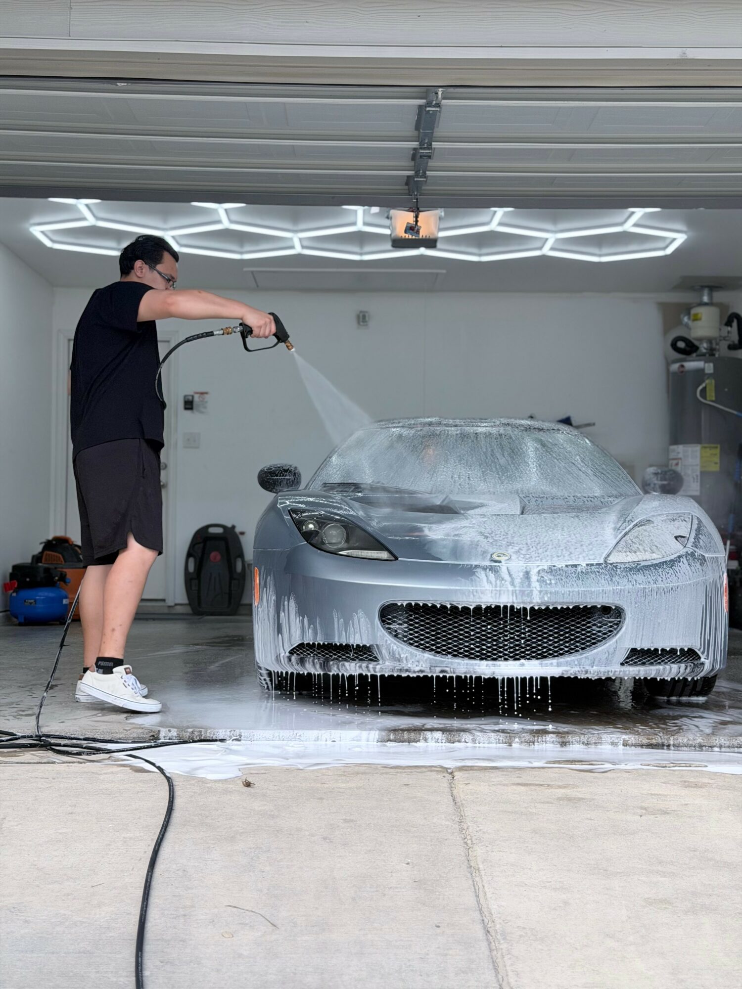 Person washing a silver sports car with foam in a garage, with a hexagonal ceiling light fixture above.