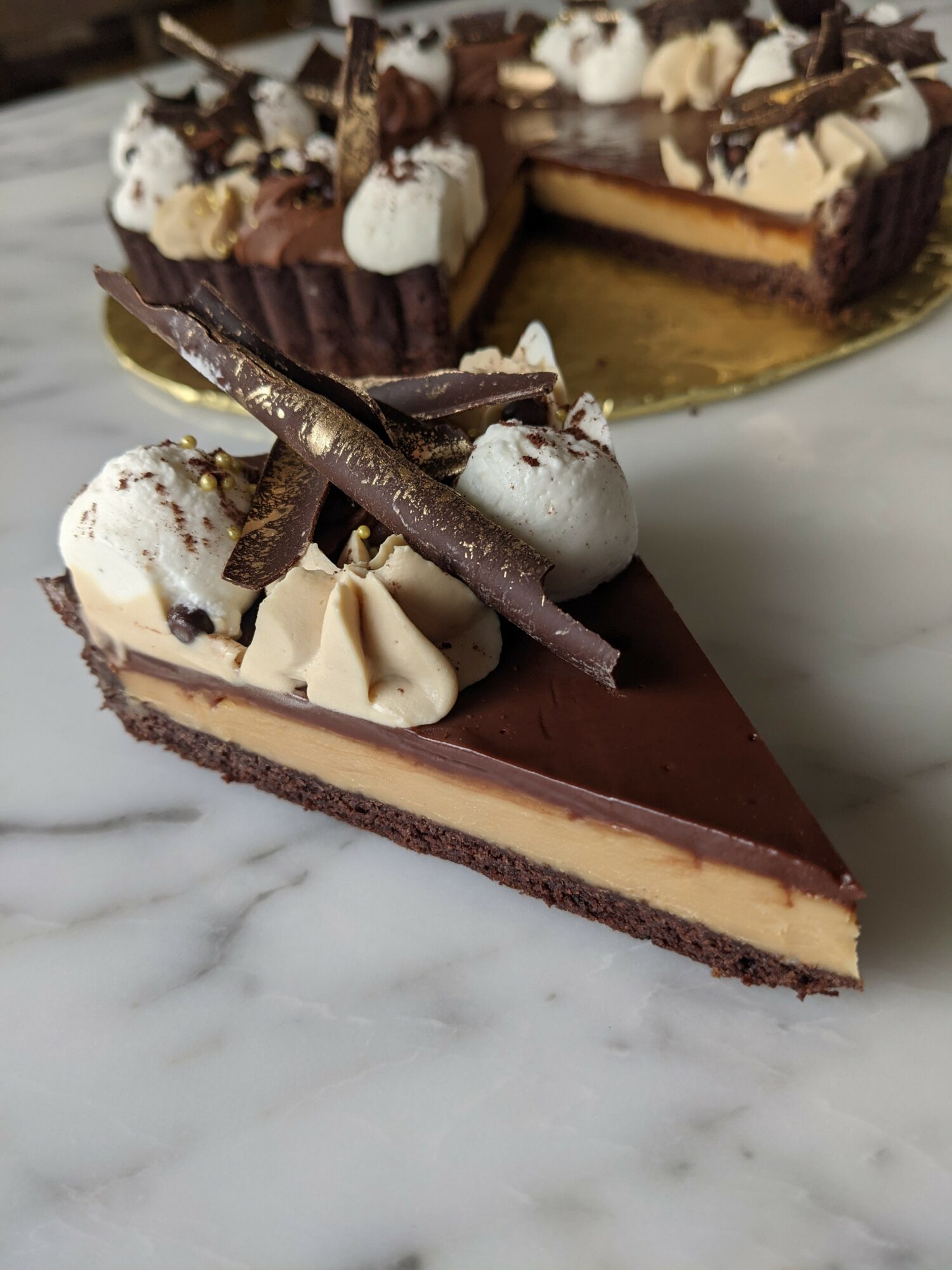 A slice of chocolate and vanilla layered cake with whipped cream, chocolate decorations, and a chocolate stick on top, on a marble surface.