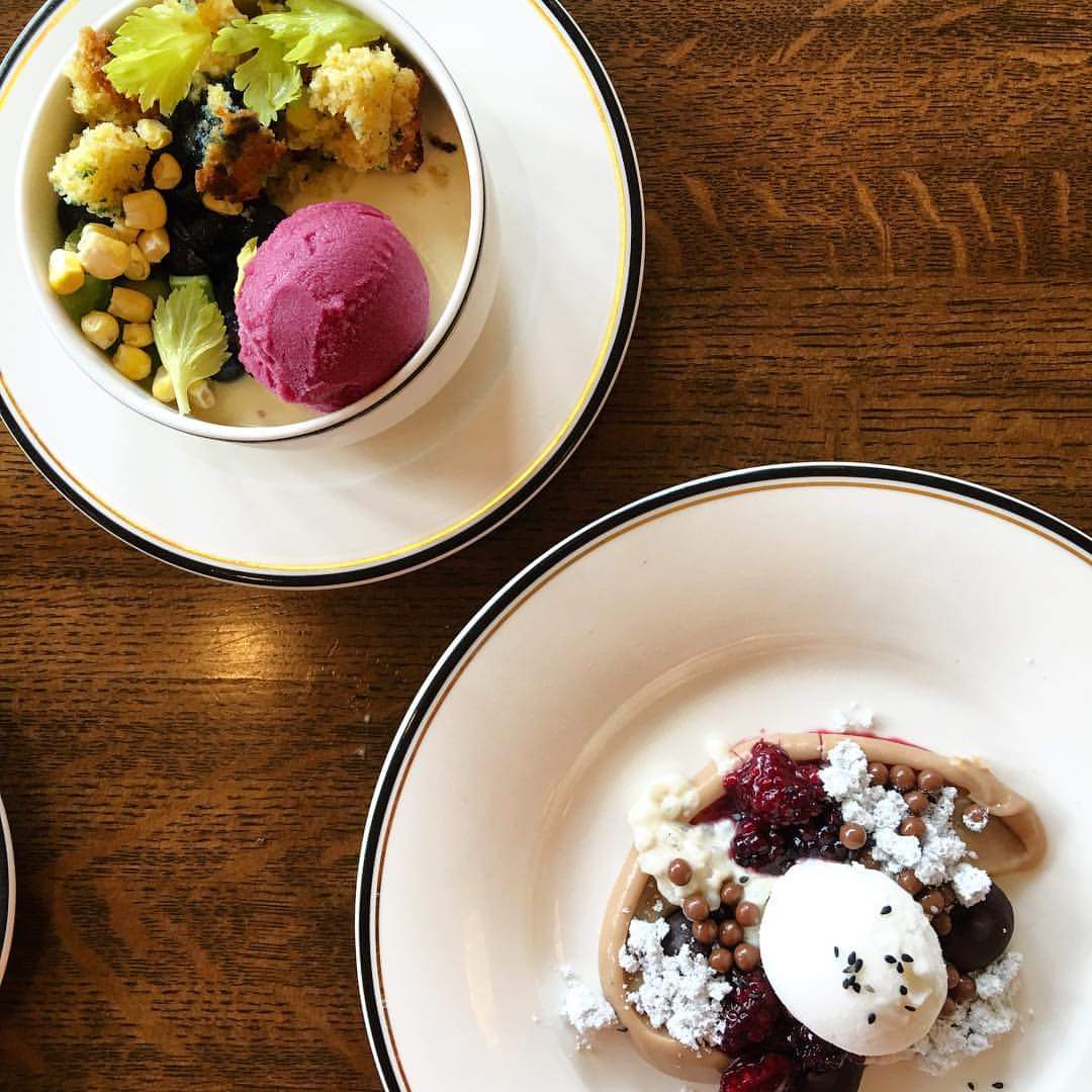 Two bowls of dessert on a wooden table, one with pink ice cream and toppings, the other with a scoop of ice cream and berries.