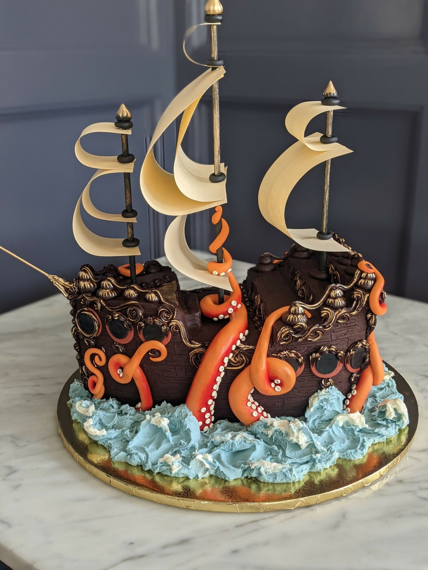 Cake decorated with chocolate and orange tentacles, with blue and white waves, on a round gold base.