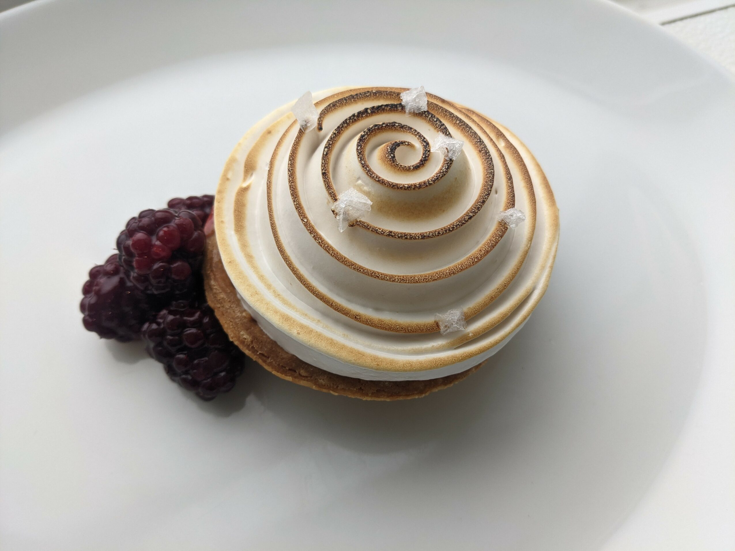 Dessert with a spiral topping and blackberries on a white plate, viewed from above.