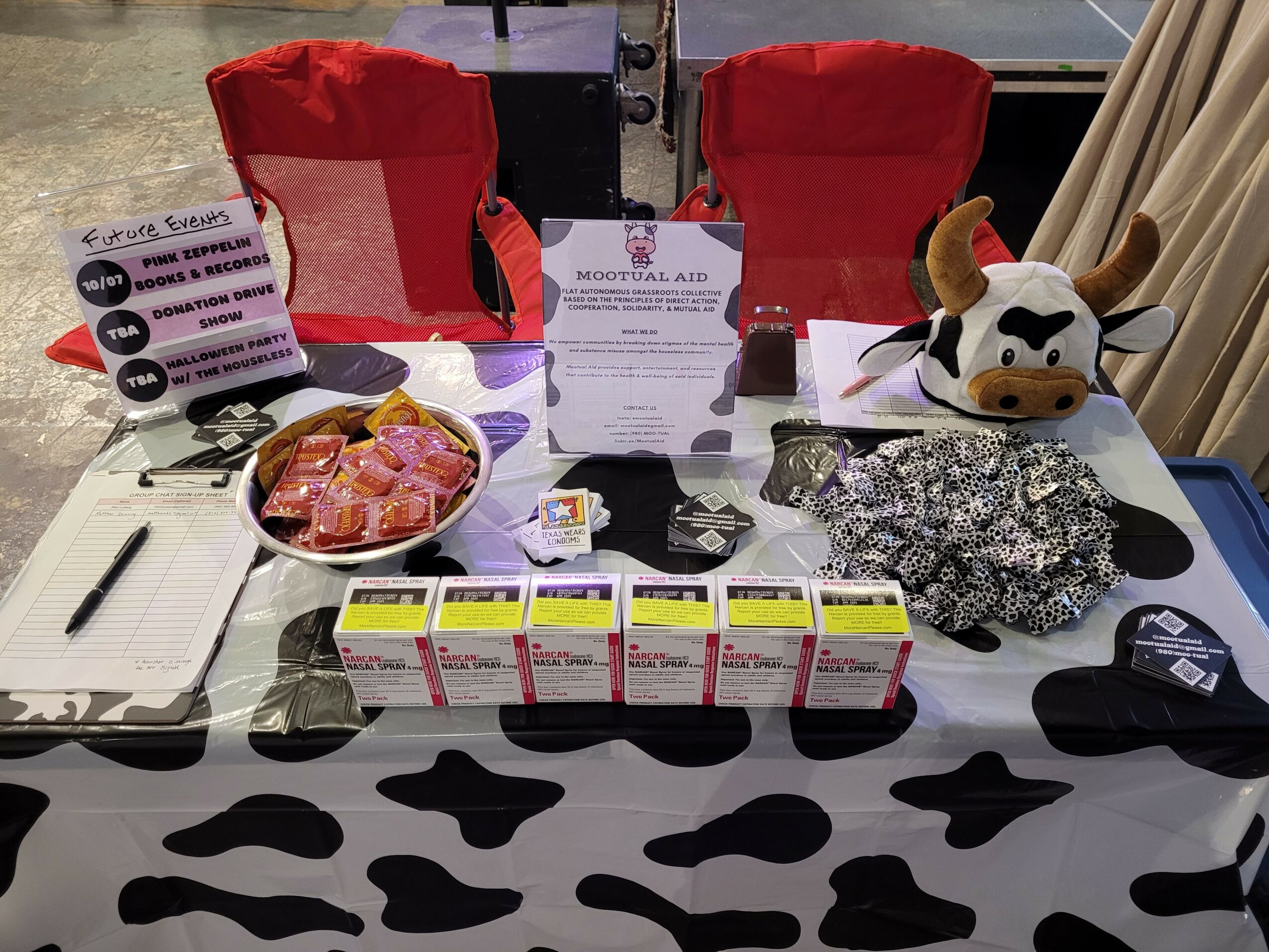 Table with red chairs, medical supplies, a plush cow, and various items on a black and white patterned tablecloth.