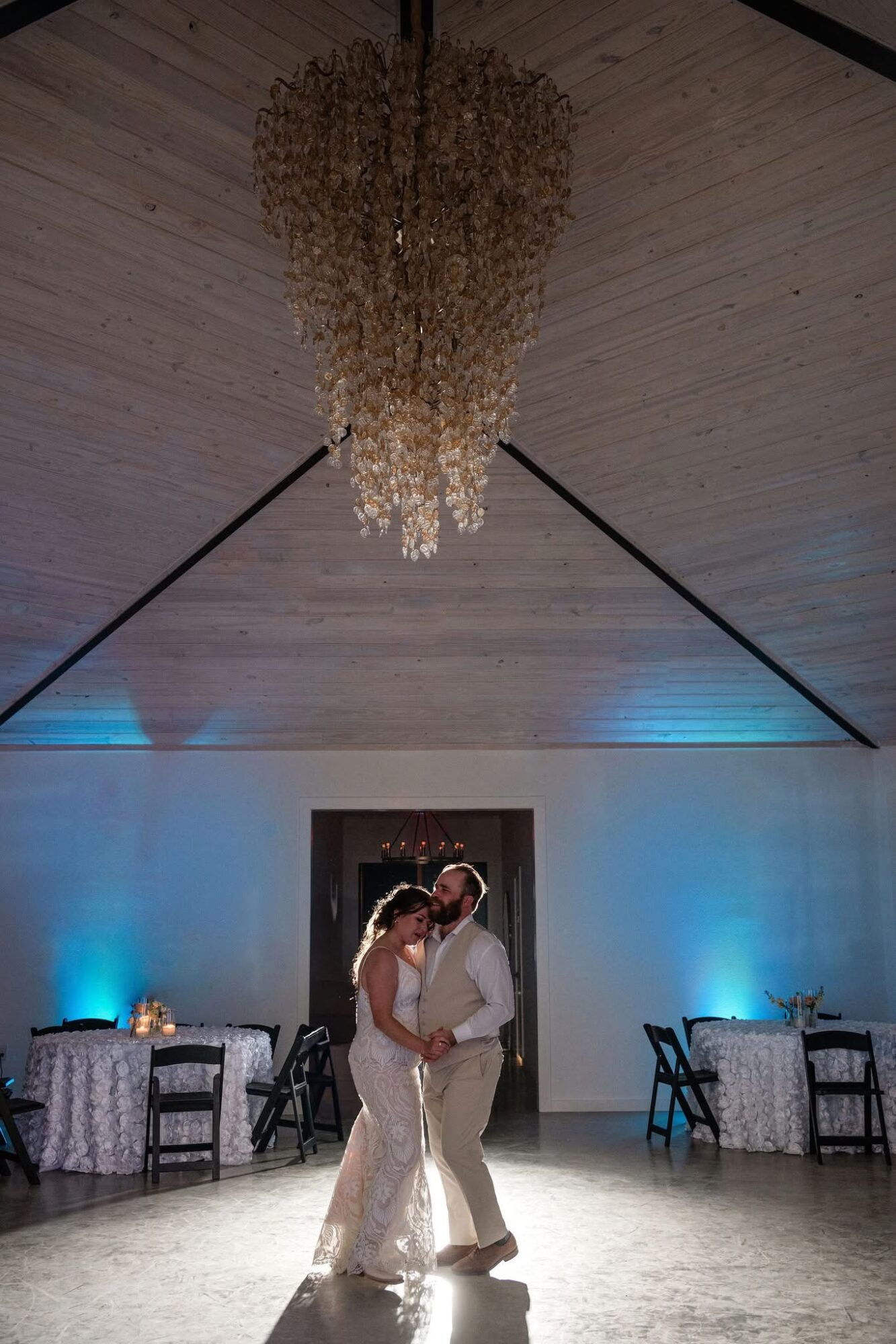 Couple dancing in a decorated room with blue lighting and a chandelier overhead.