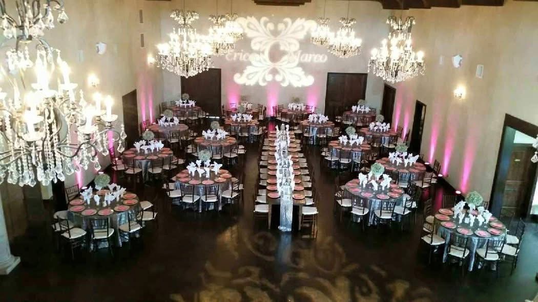 Elegant banquet hall with chandeliers, round tables, and pink lighting, set for a formal event.