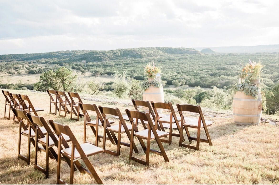Multiple wooden chairs arranged outdoors on a grassy hill with a scenic landscape in the background.