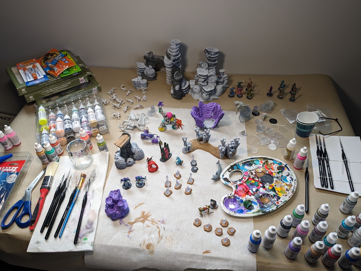 Art supplies and miniature figures on a table, including paint bottles, brushes, and sculpting materials.