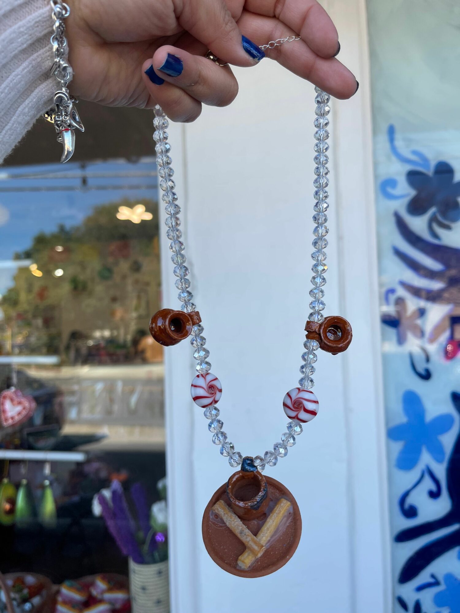 Hand holding a beaded necklace with brown and pink beads, and a large round pendant, against a background of a window and outdoor scene.