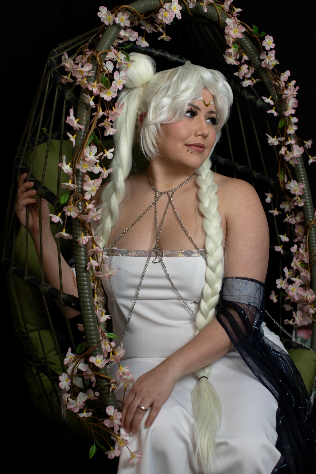Person with long white braided hair in a white dress, surrounded by a floral swing, looking to the side.